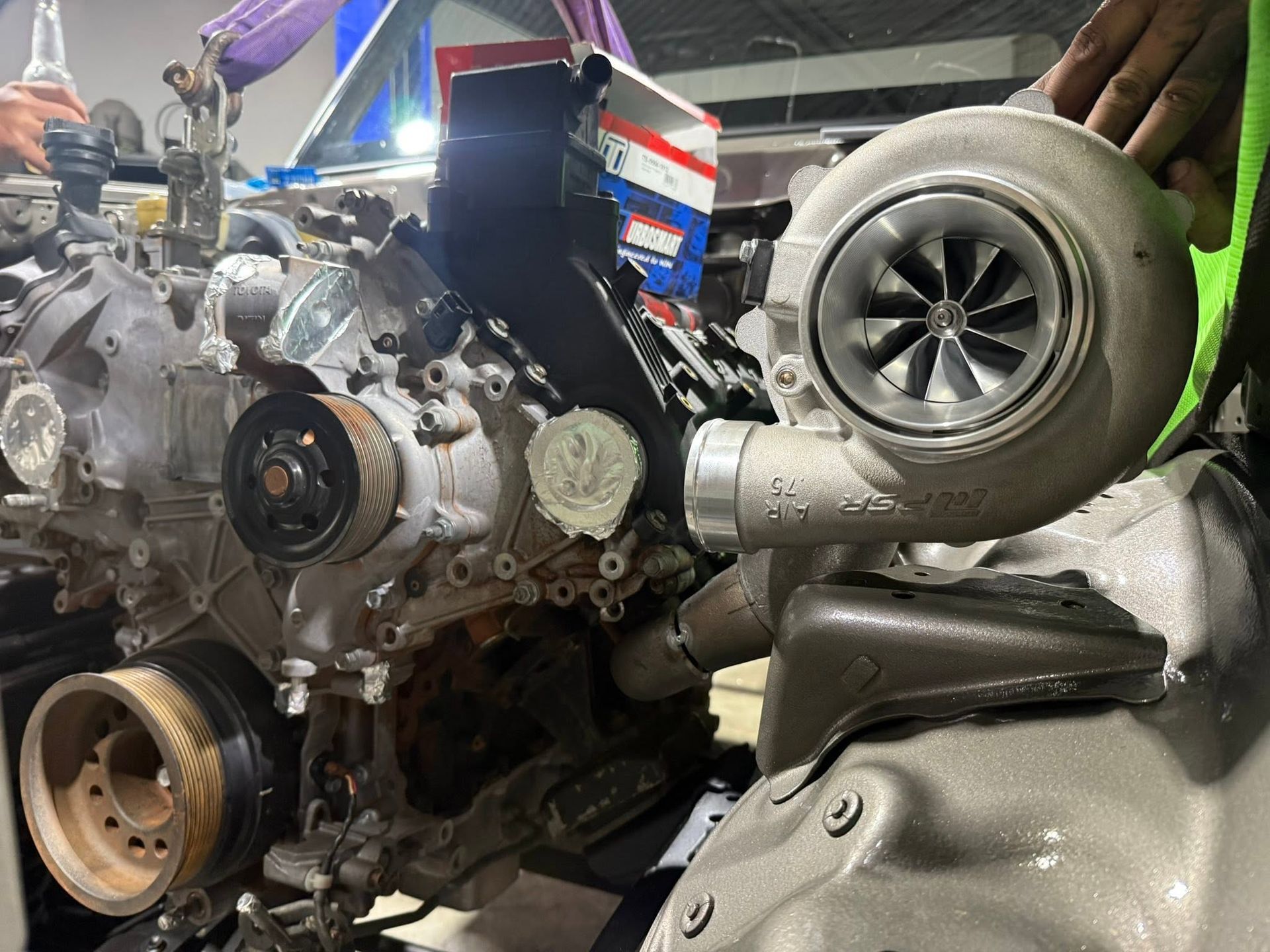 Turbocharged engine on a workbench, with large silver turbo and visible engine components in a garage.