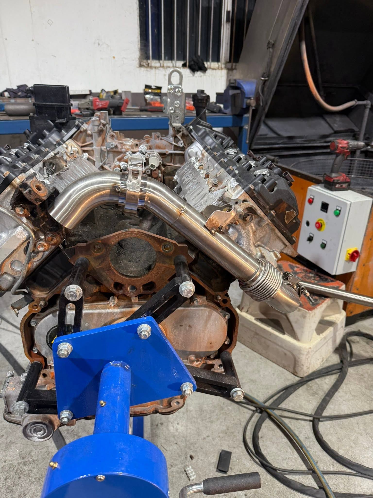 V8 engine on a test stand with shiny exhaust pipes and a blue mount in a workshop