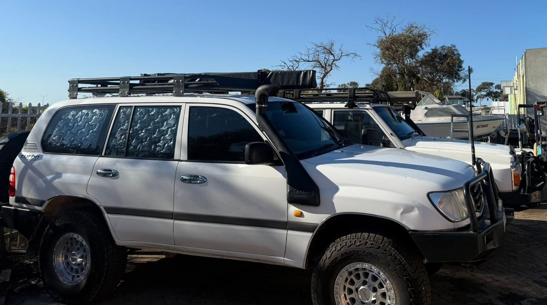 White SUV with roof rack and front bull bar parked in a lot, viewed from the side.