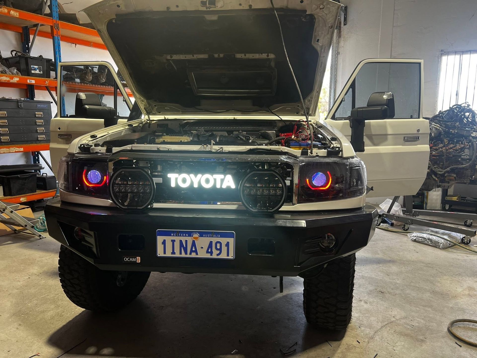 Black Toyota SUV in a garage with hood open and headlights on, front view.