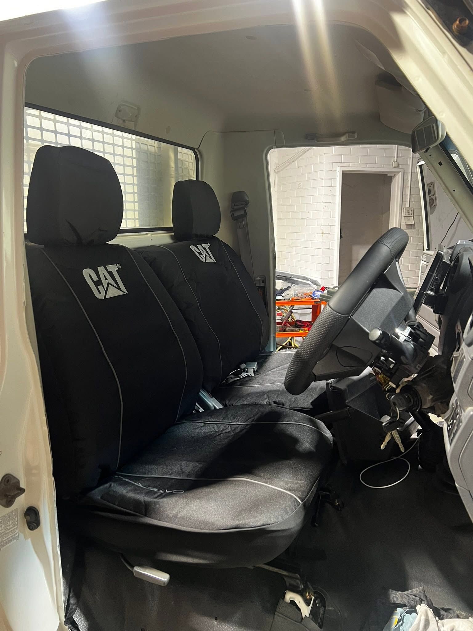 Truck cab interior with black CAT seat covers, steering wheel, and windshield lit by sunlight