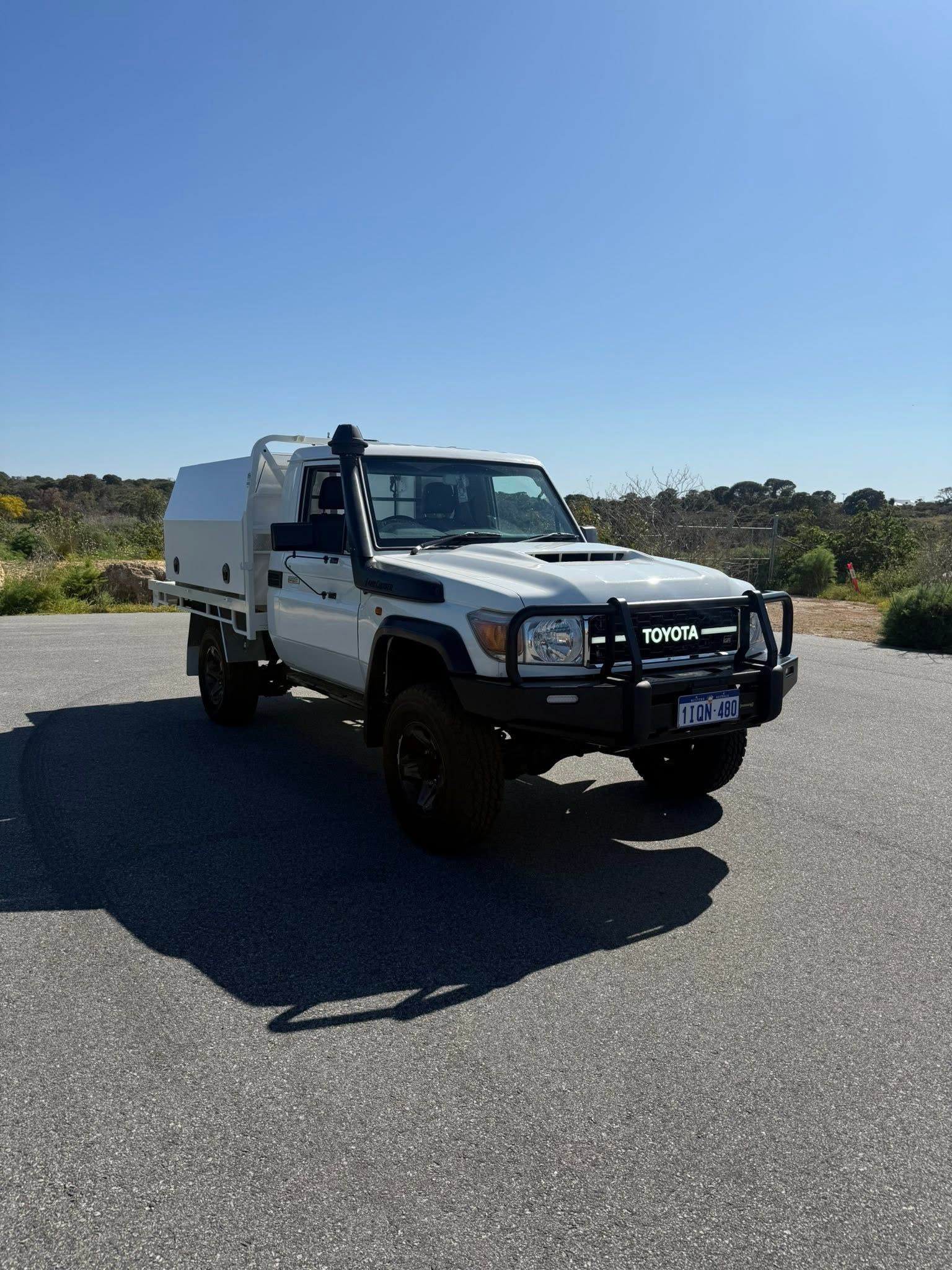 White utility truck on a sunny road with a person standing by the cab.