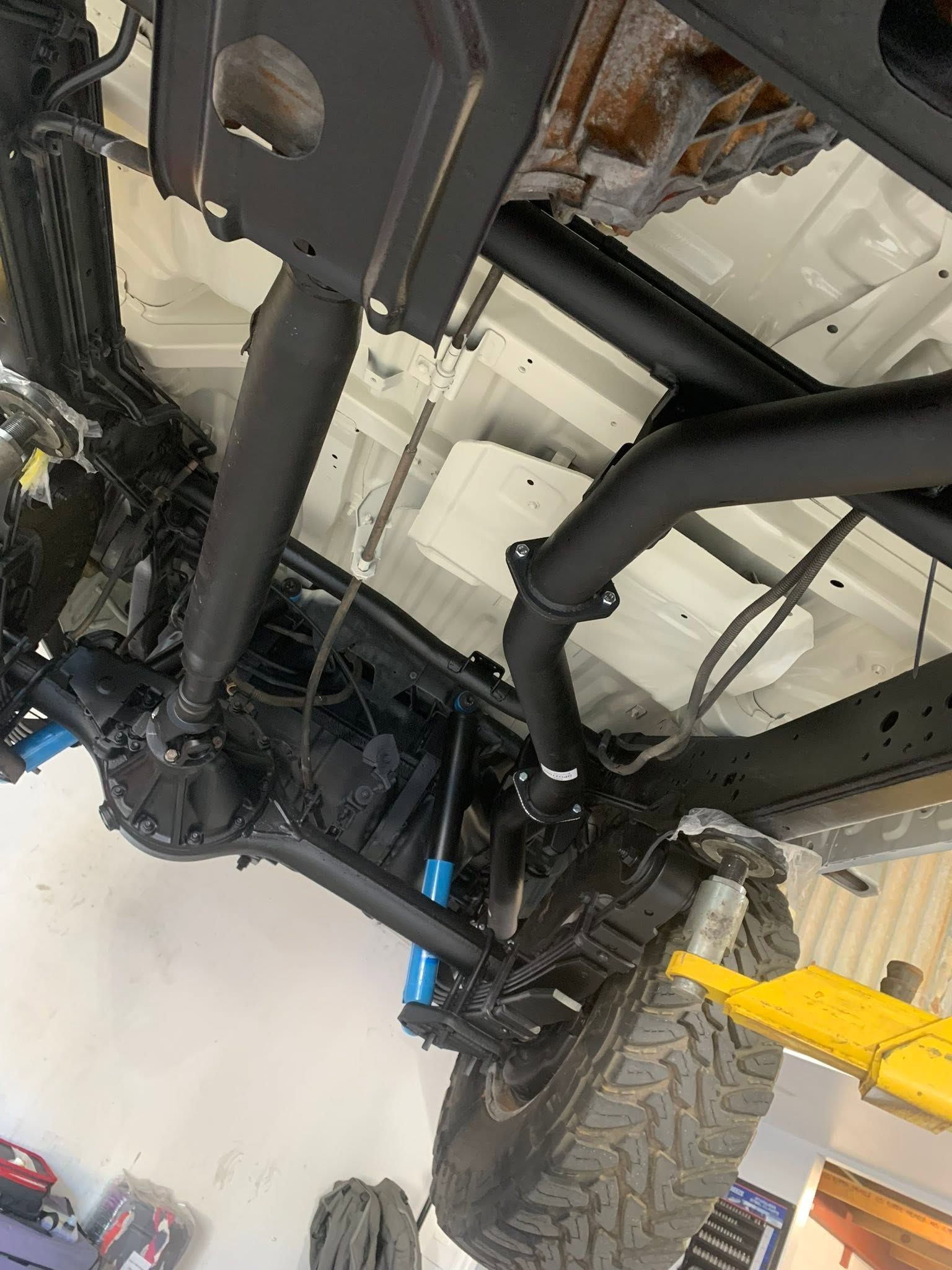 Undercarriage of a lifted off-road truck with black suspension parts and yellow jack support