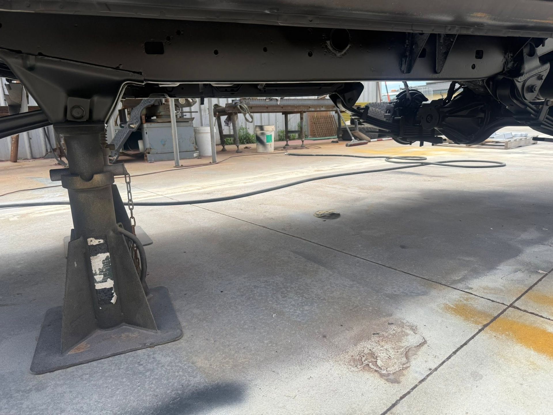 Undercarriage of a vehicle on jack stands in a garage or driveway, with a wheel removed.