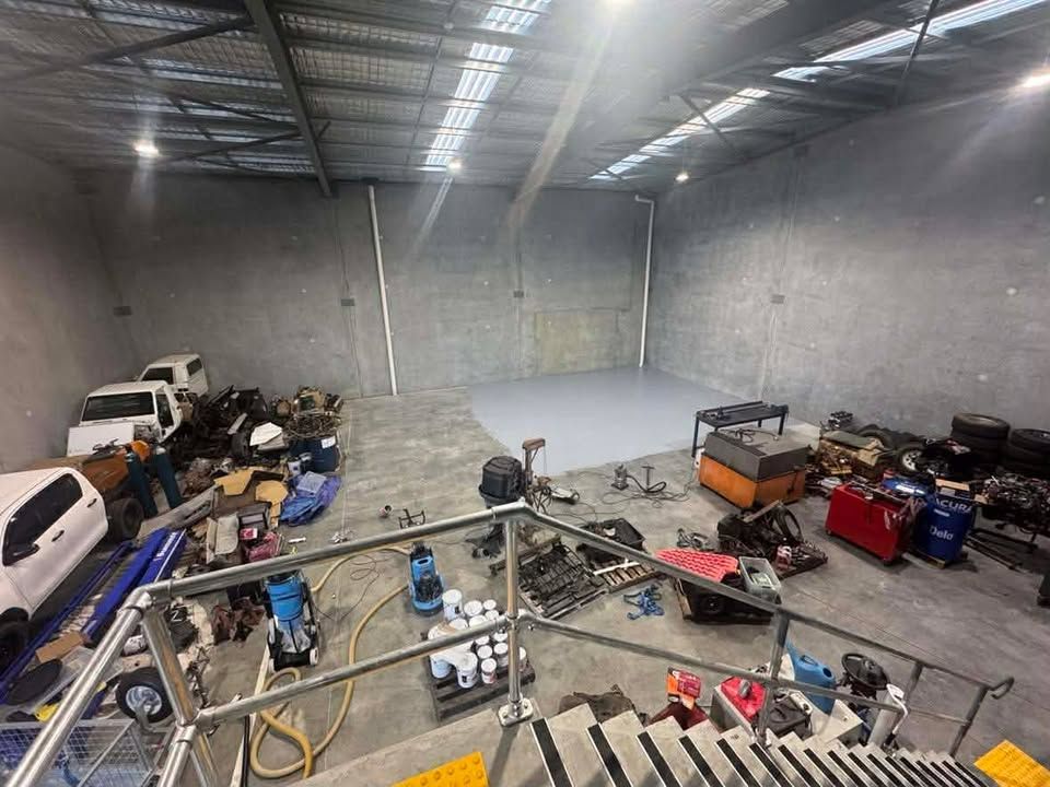 Large empty warehouse with metal fencing, parked vehicles, tools, and equipment scattered along the walls.
