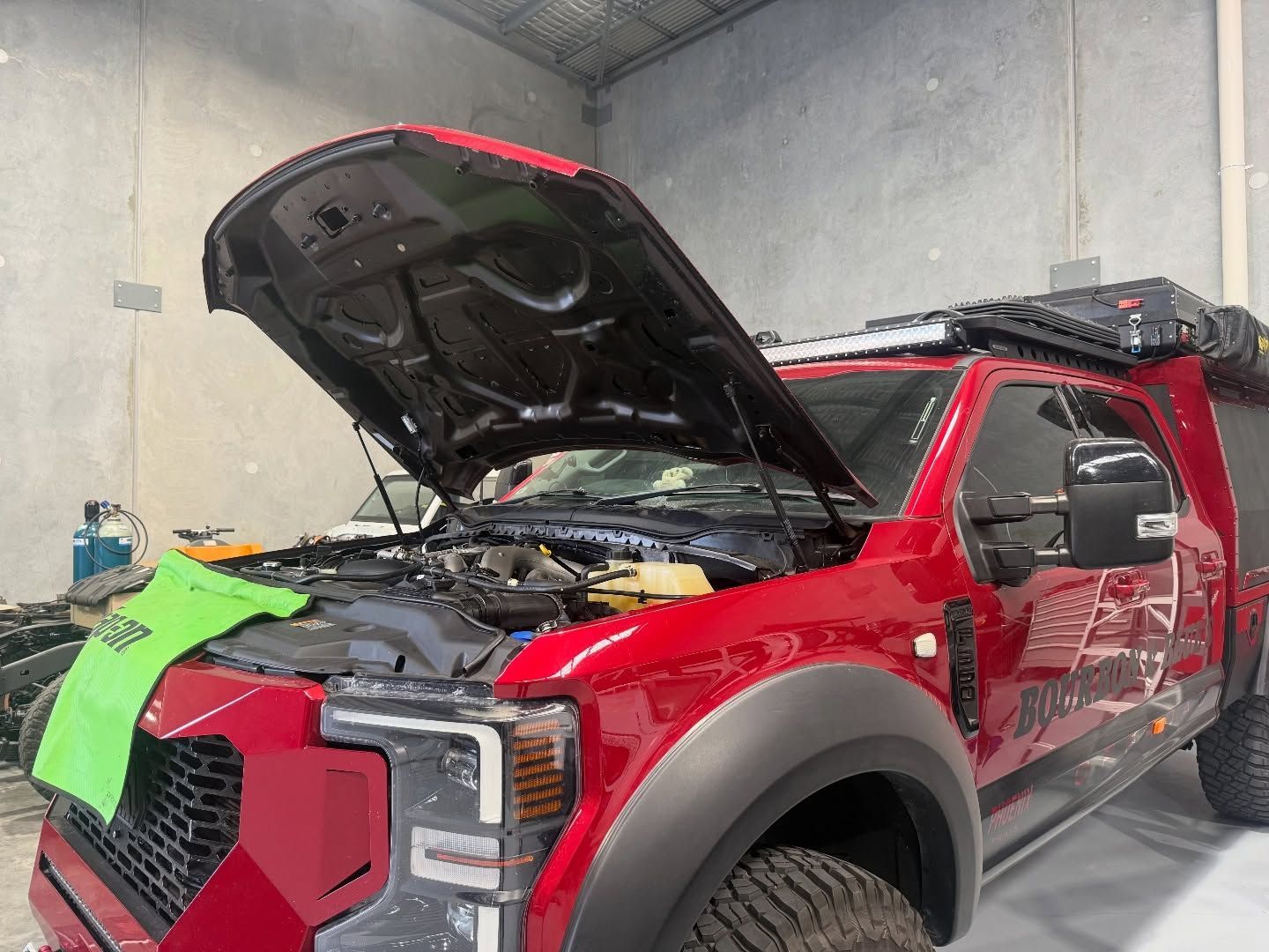 Red pickup truck in a garage with hood open and front end stripped for repair