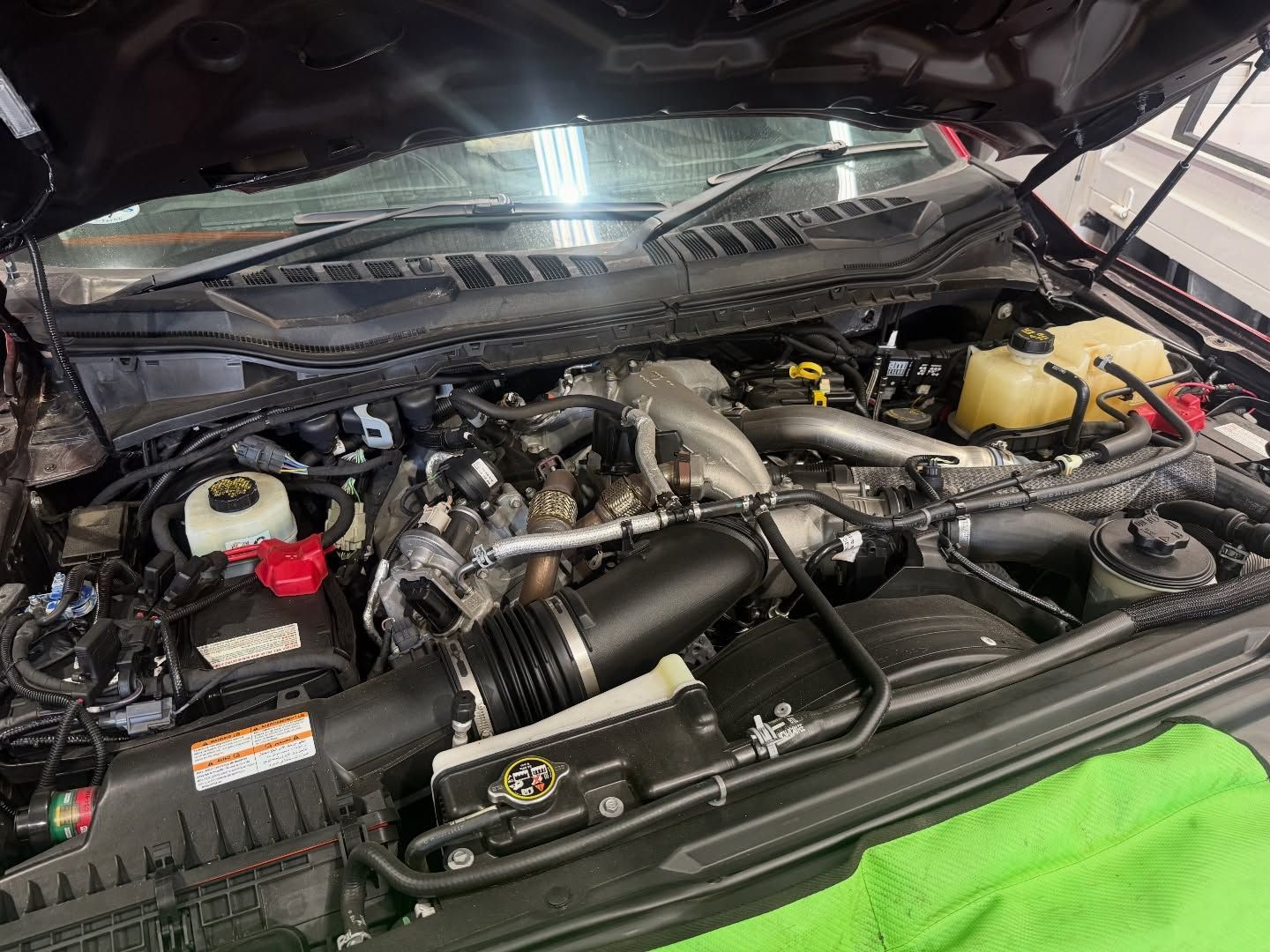 Close-up of an engine bay with visible hoses, air intake, and fluid reservoirs under an open hood.