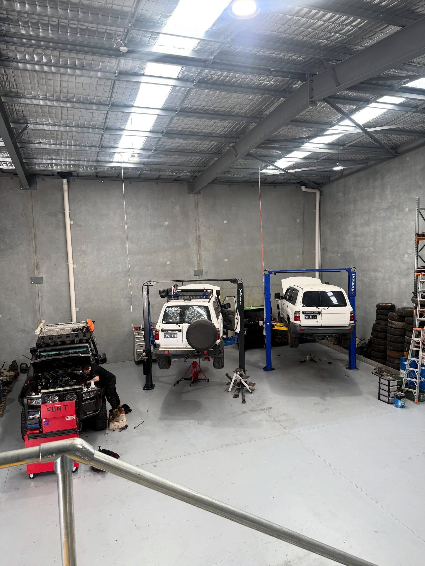 Auto repair garage with two white vehicles, a red engine, and tools under a metal roof