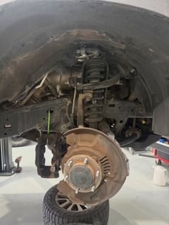Car wheel removed, showing brake rotor, suspension, and wheel well on a vehicle lift