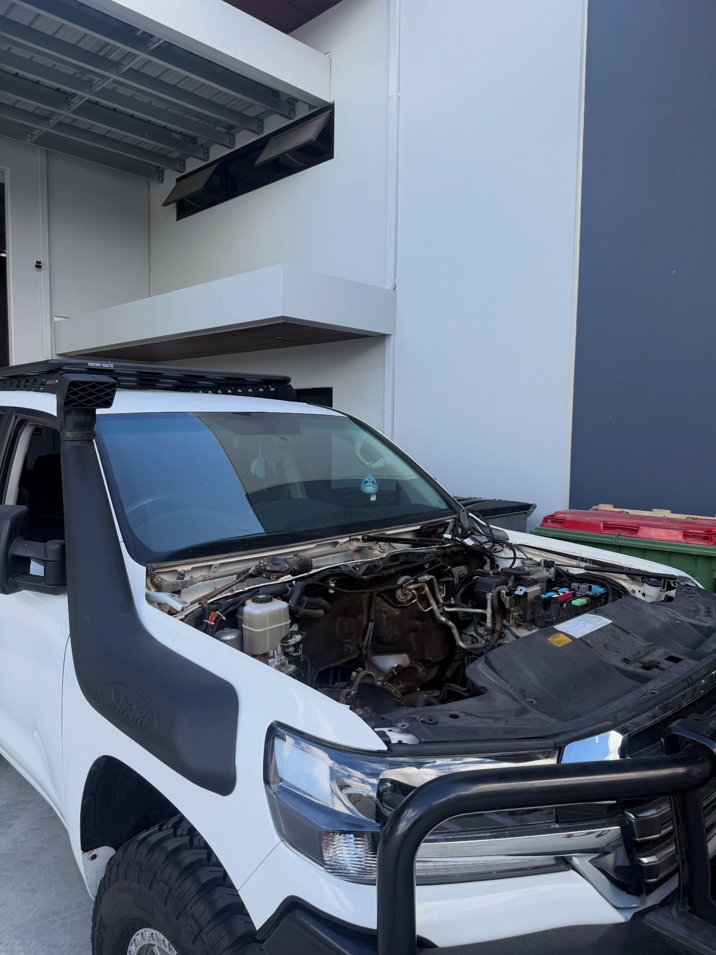 White pickup truck with hood removed, exposing engine, parked outside a building loading bay