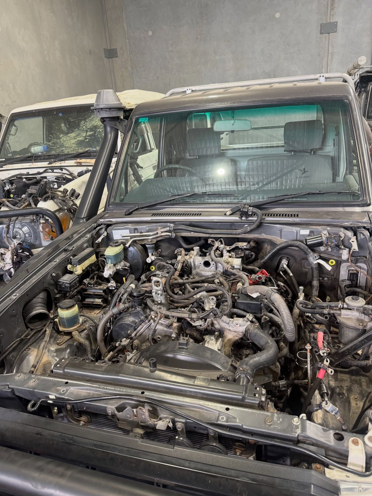 Two SUVs in a garage, with the front one stripped to its engine bay.