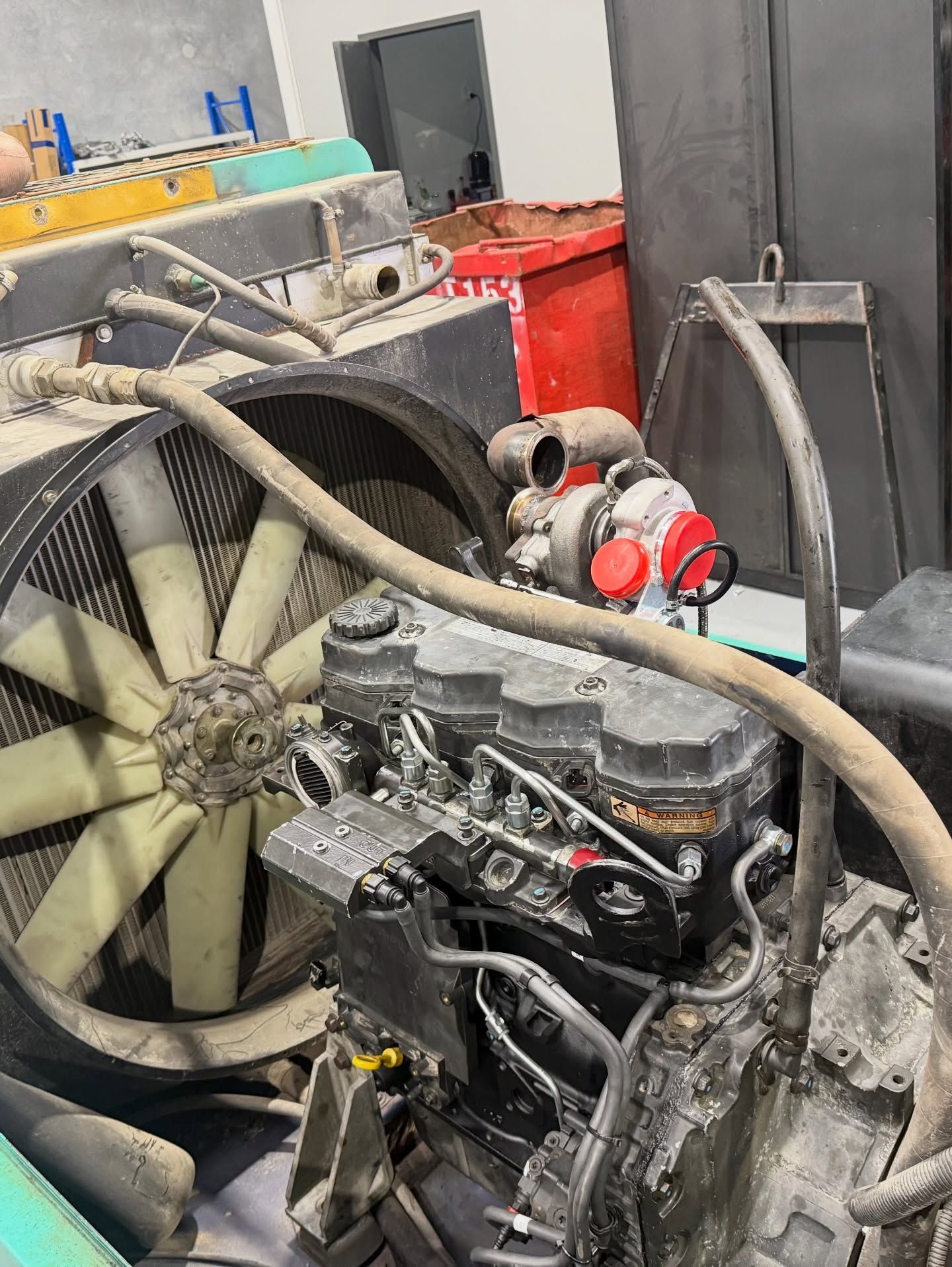 Industrial engine with large fan and hoses in a workshop, showing mechanical equipment and red components.