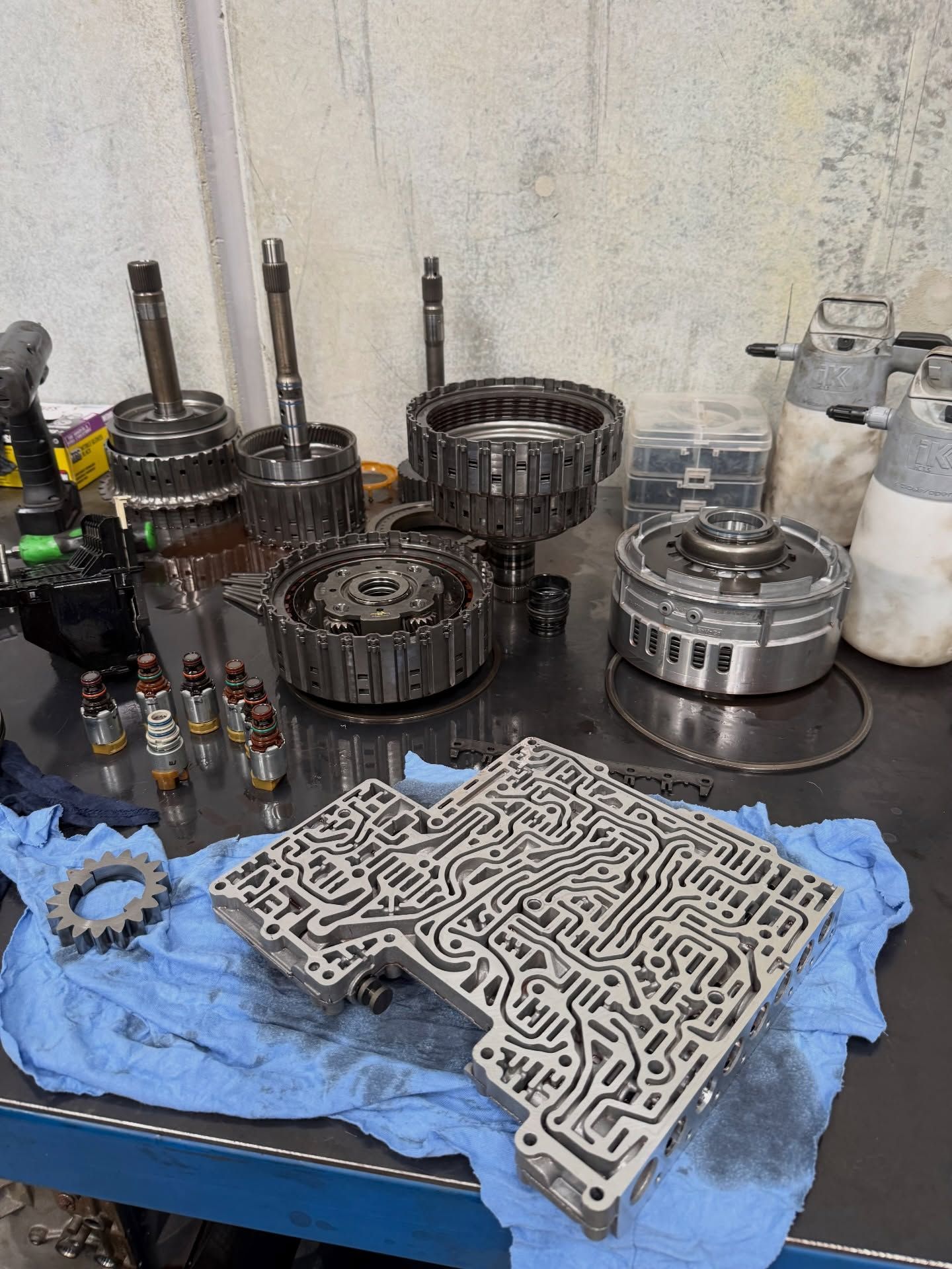 Assorted auto transmission parts and gaskets arranged on a blue cloth in a workshop.