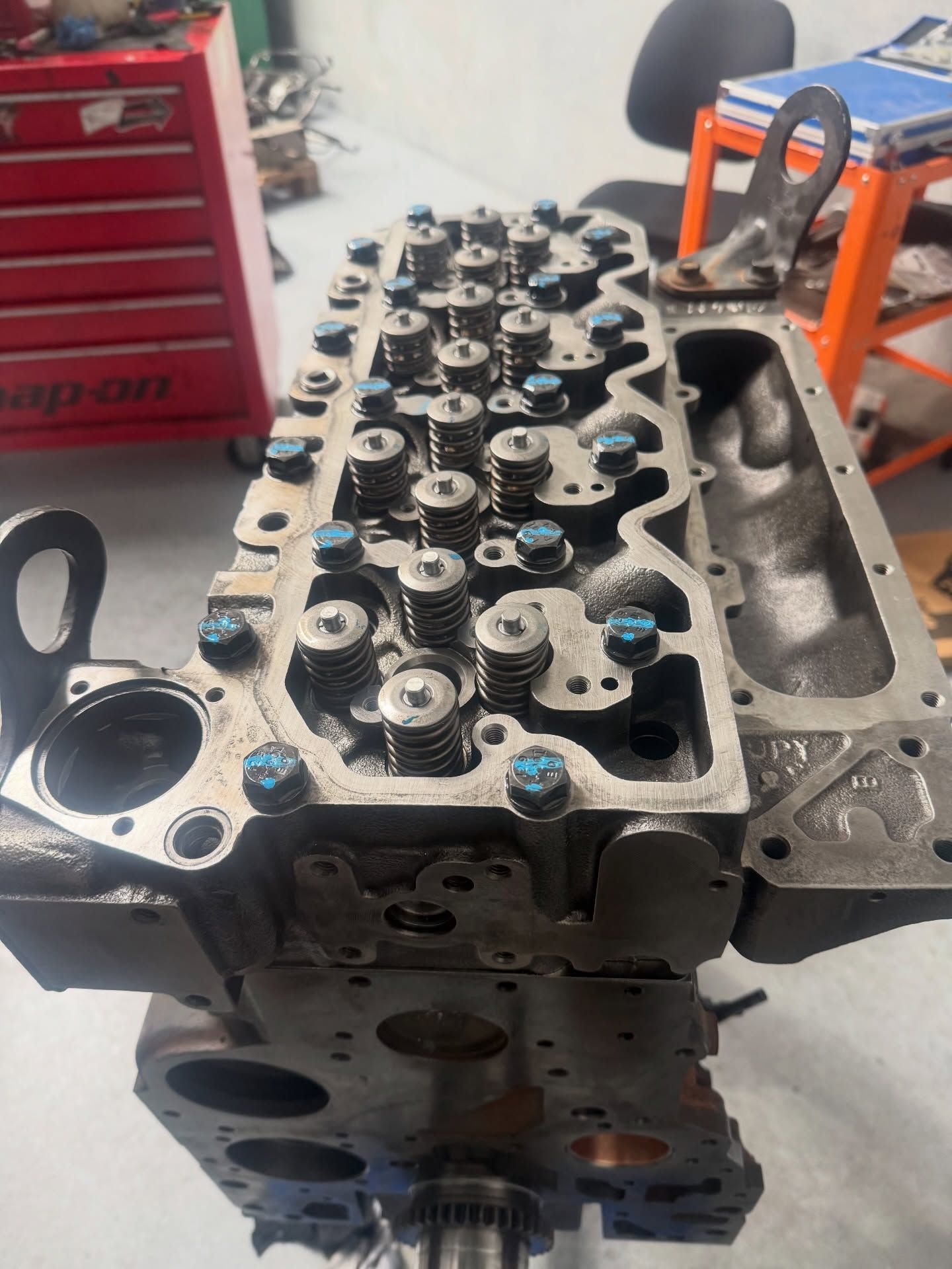 Automobile engine cylinder head on a workbench, with valve springs and a red tool chest in the background