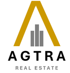 Het logo van AGTRA Real Estate met een goudkleurig dak en grijze gebouwen boven zwarte tekst.