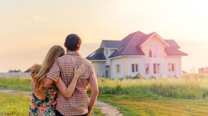 A man and woman are hugging in front of a sold sign.