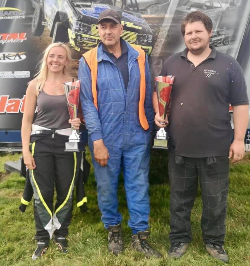 Two men and a woman holding trophies in front of a sign that says ' racing ' on it