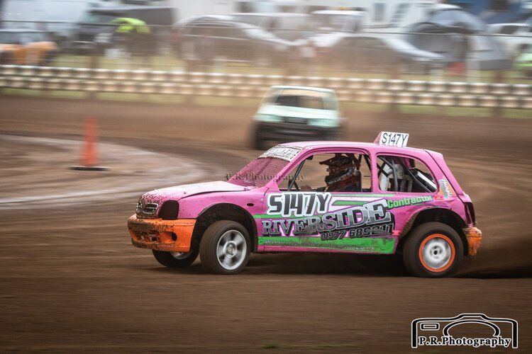 A pink and green race car is driving on a dirt track.