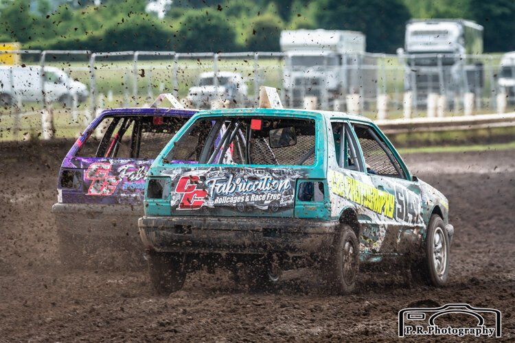 Two cars are racing in the mud on a dirt track.