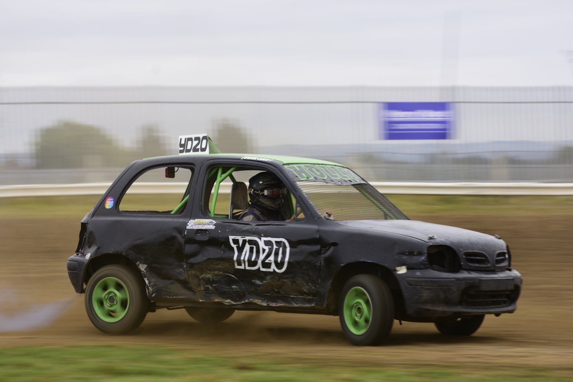 A black and green race car is driving on a dirt track.