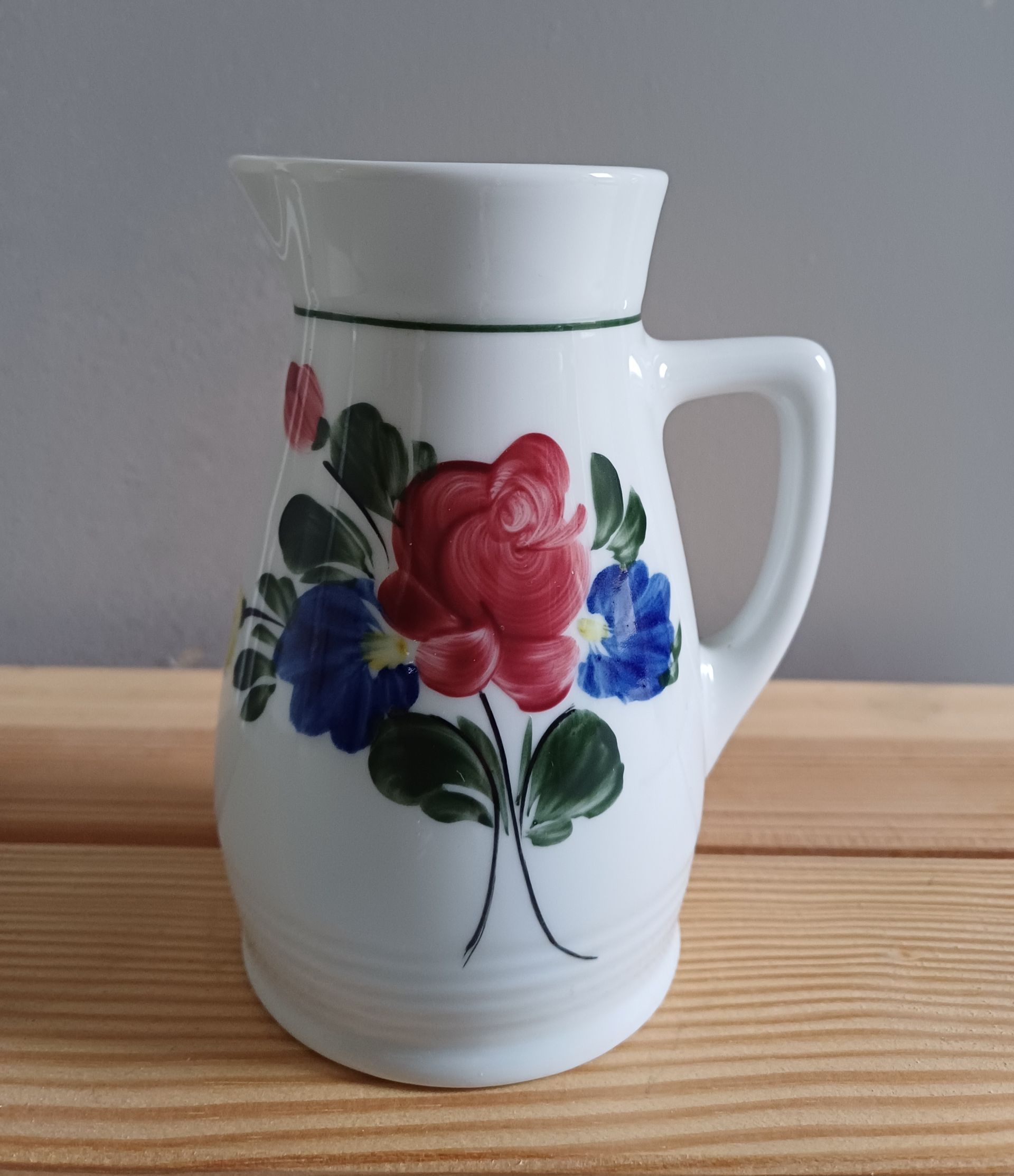 Witte keramische kan met een rood en blauw bloemenmotief.