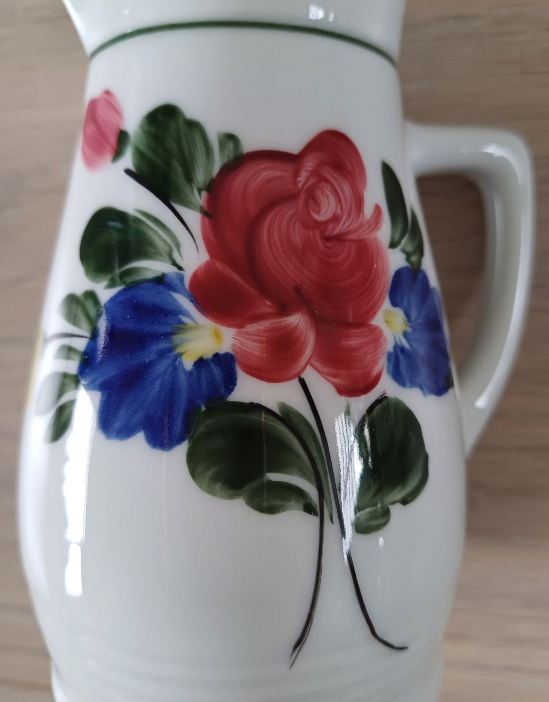 Witte keramische kan met een rood en blauw bloemenmotief.