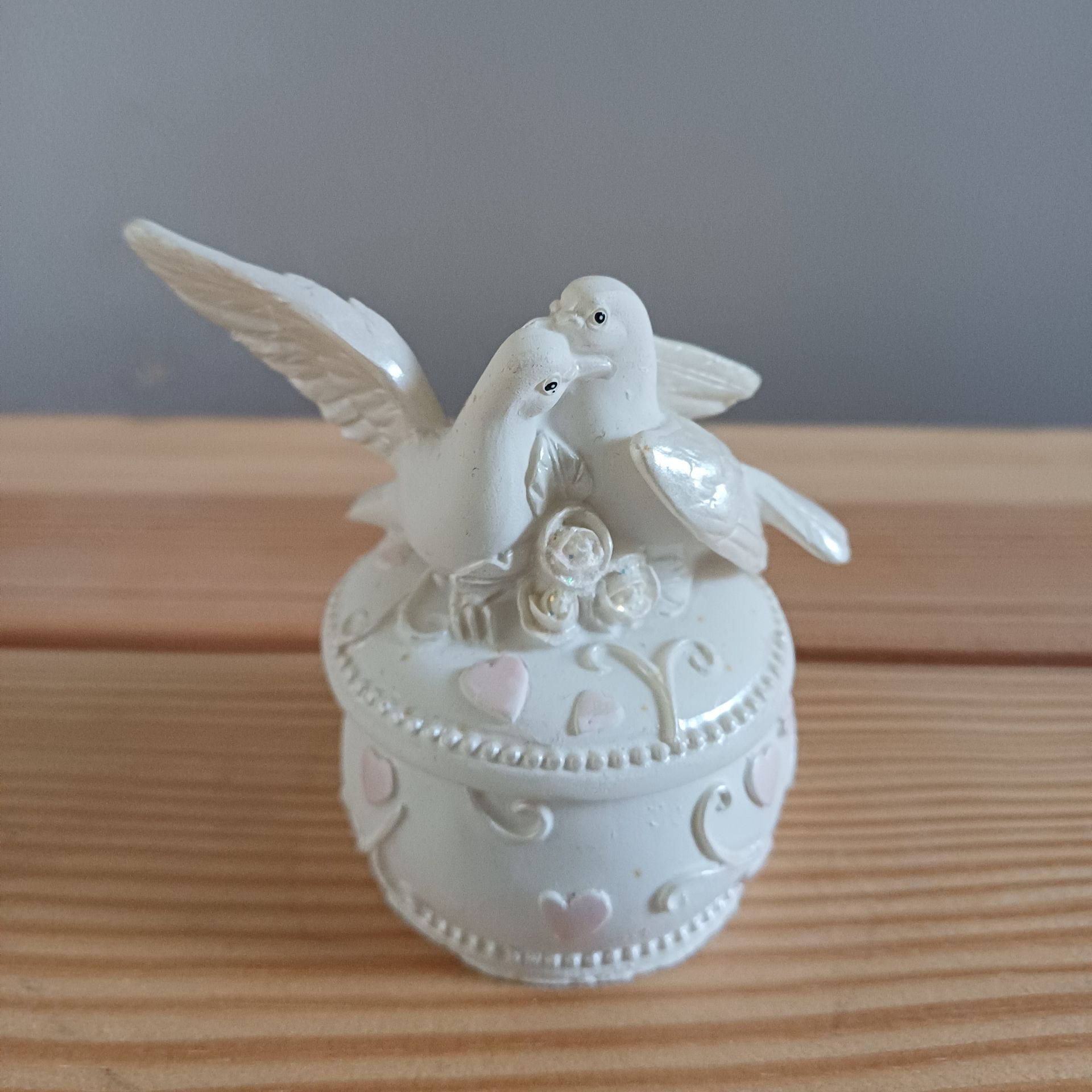 Witte keramische doos met twee duiven erop, versierd met roze hartjes.