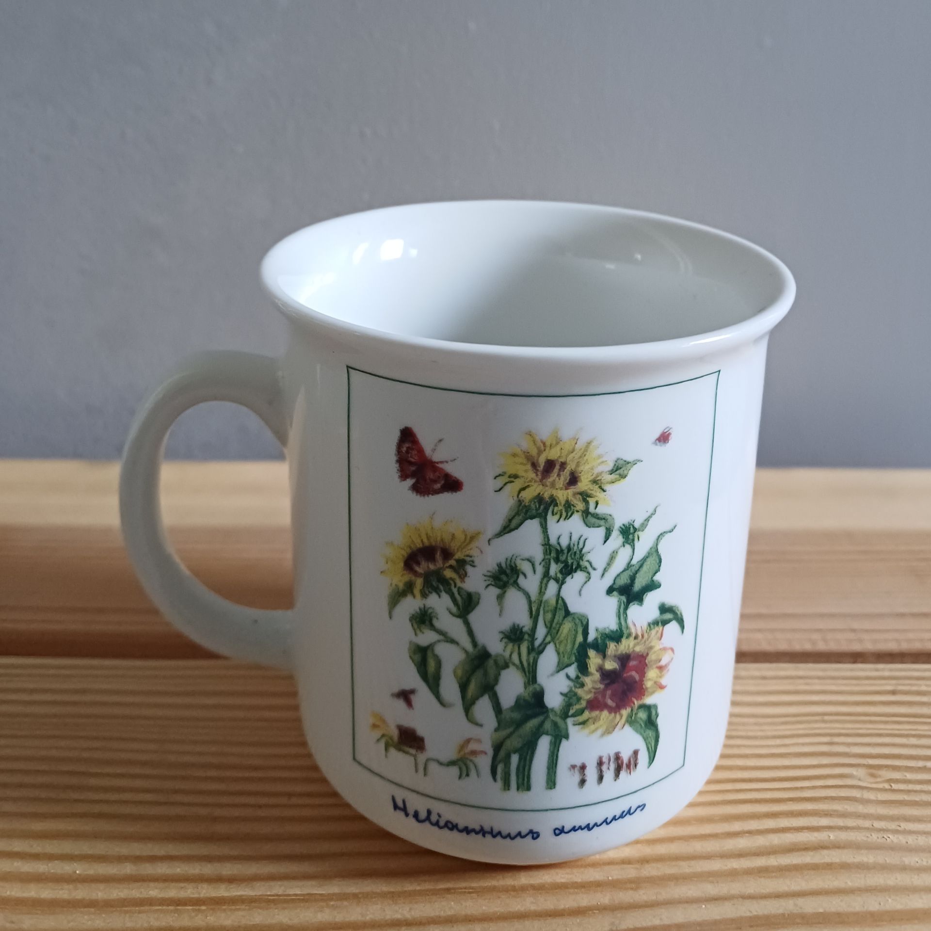 Witte mok met zonnebloemillustratie, die op een houten ondergrond staat.