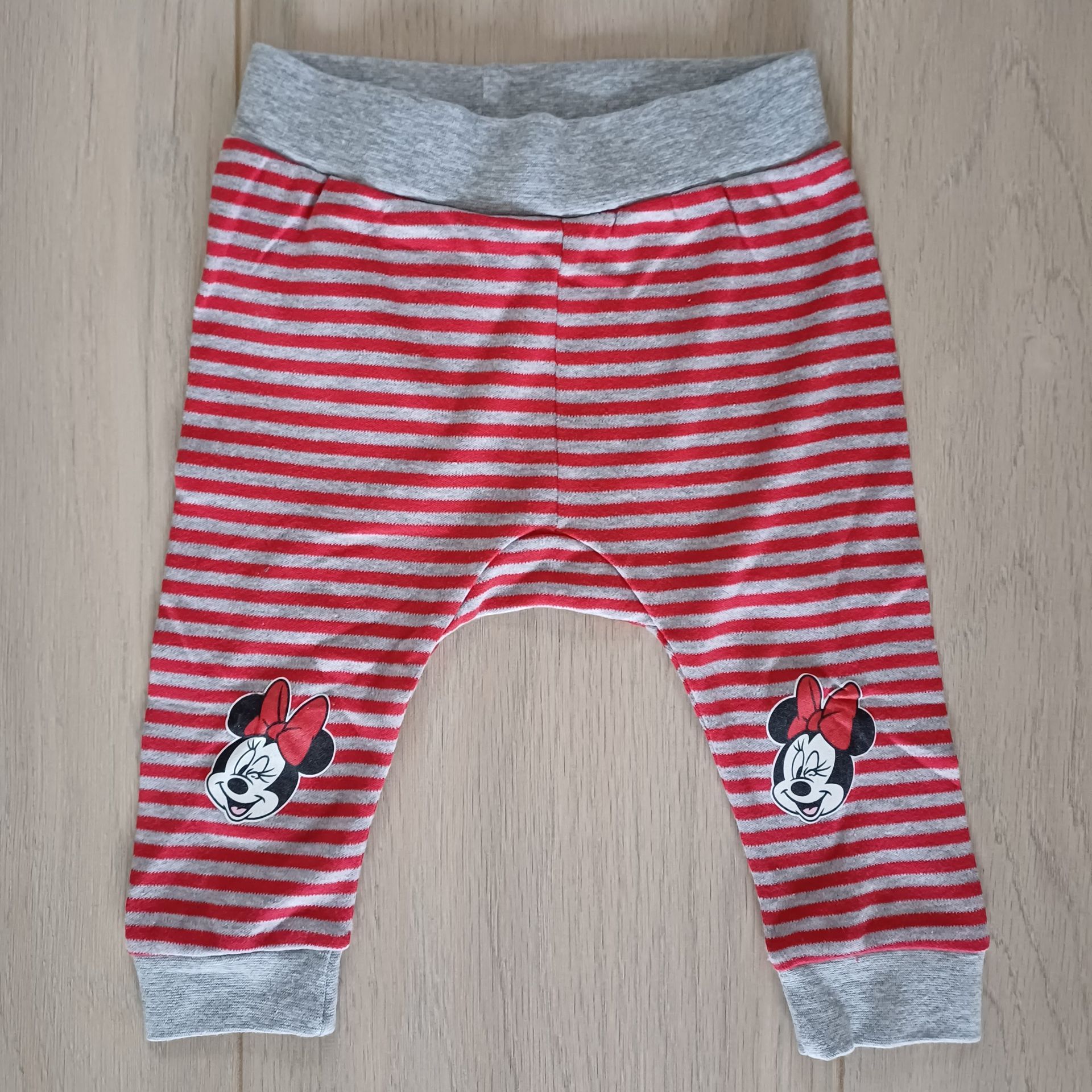 Rood-wit gestreepte babybroek met grijze tailleband en boorden. Met Minnie Mouse-gezichtjes op beide broekspijpen.