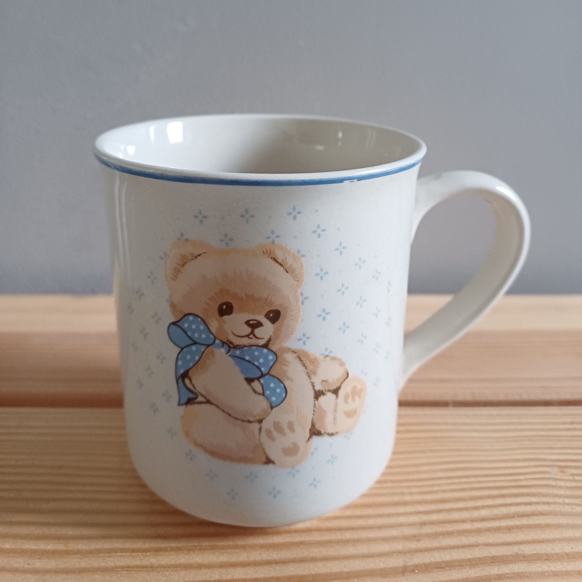 Witte keramische mok met teddybeerontwerp en blauwe accenten.