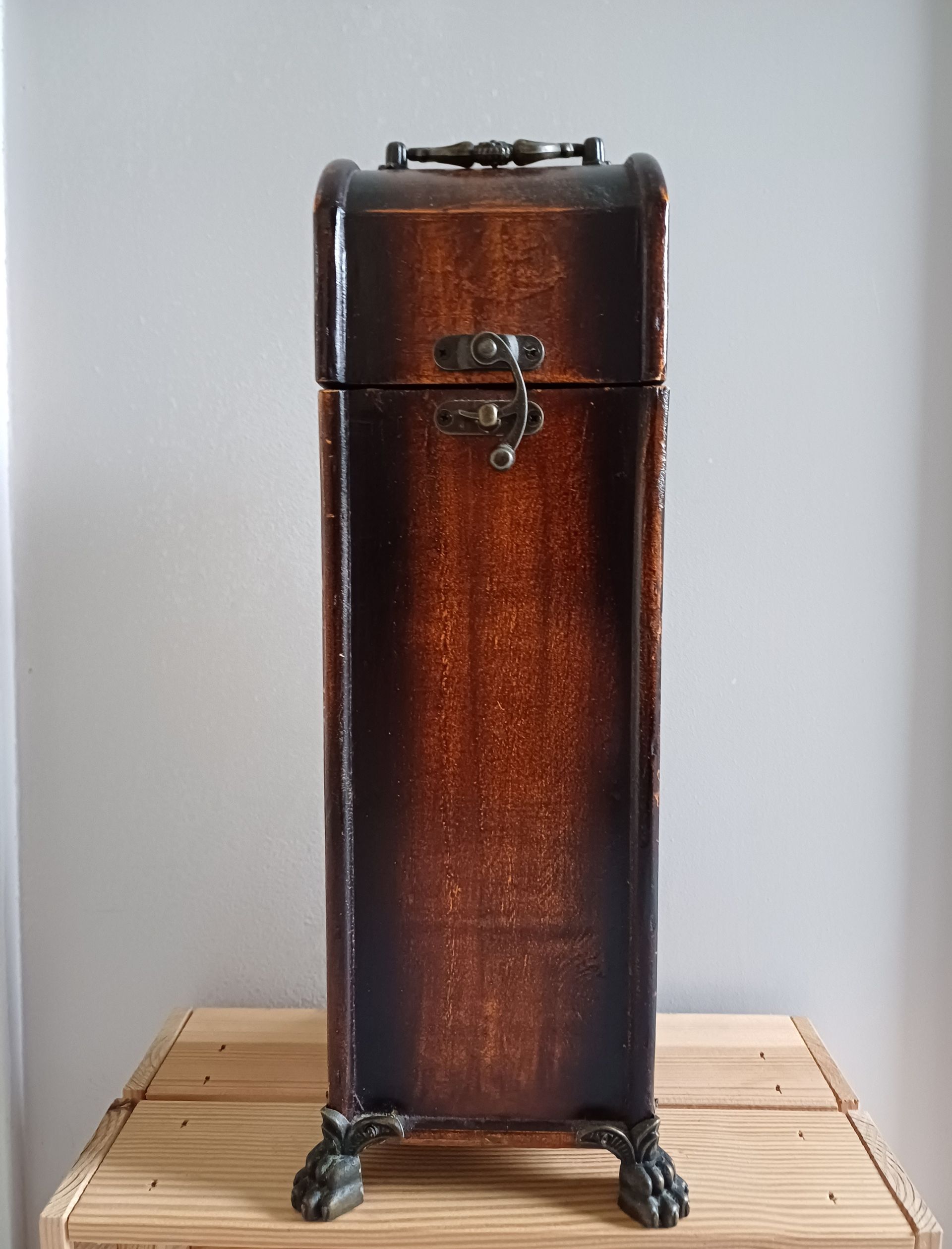 Vintage houten wijnkoffer met sierlijke sluiting en handgreep, rustend op decoratieve klauwpoten.