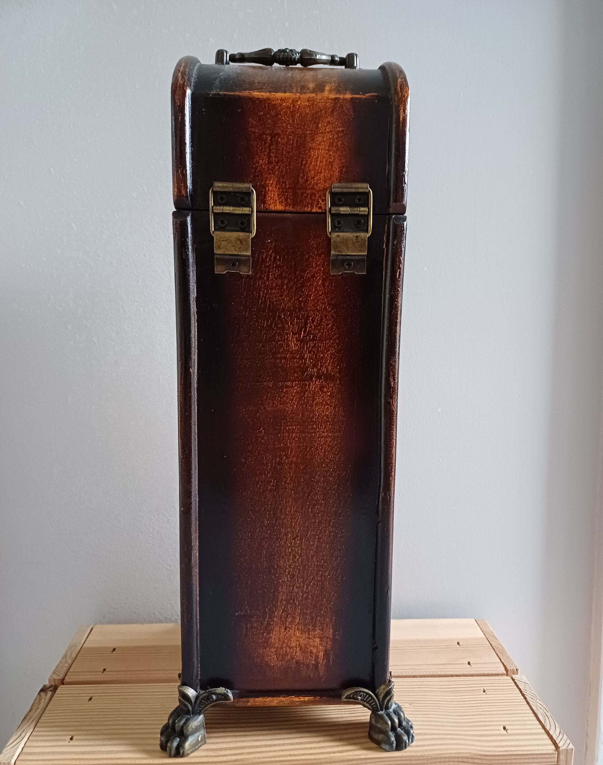 Vintage houten wijnkoffer met sierlijke sluiting en handgreep, rustend op decoratieve klauwpoten.