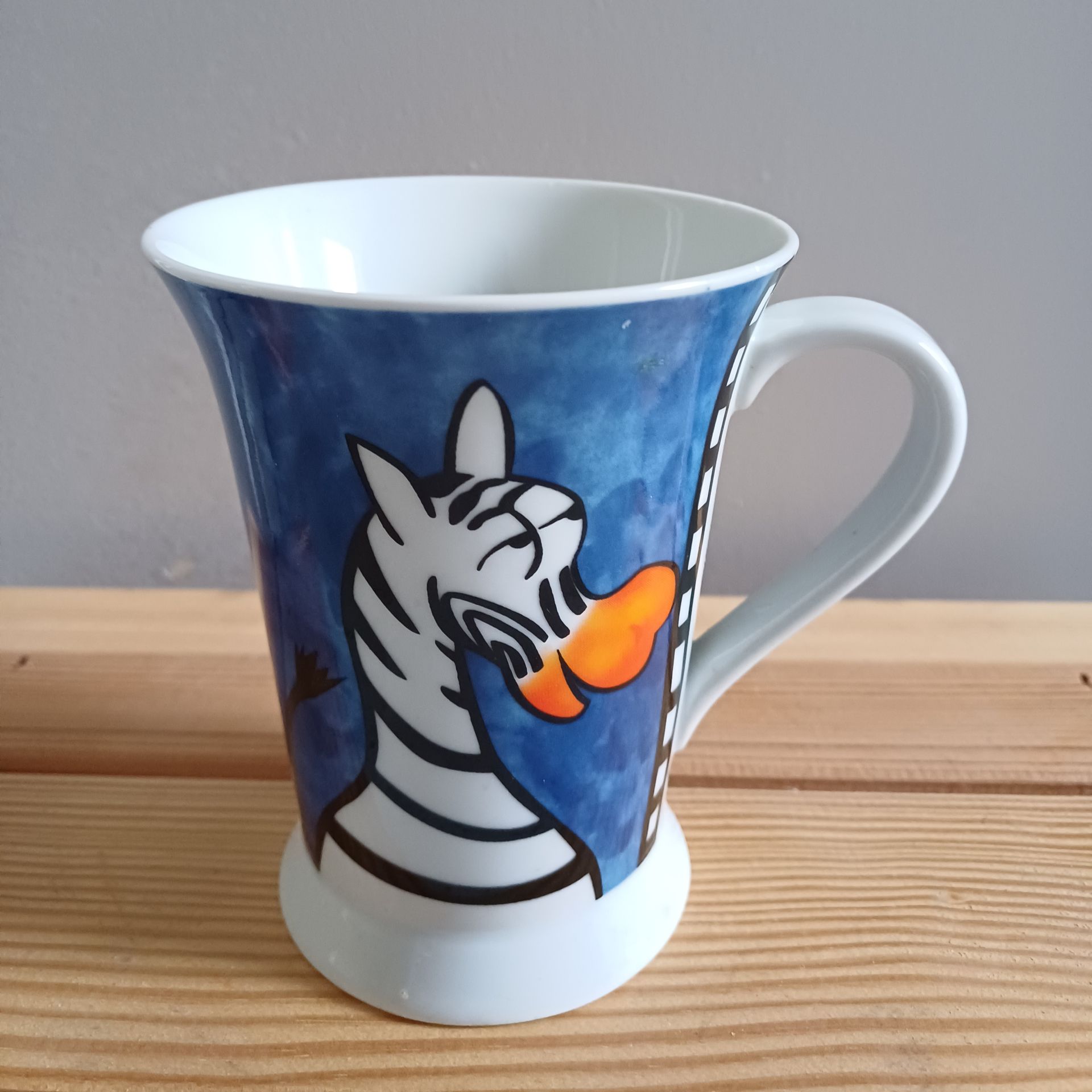 Mok met een cartoonzebra op een blauwe achtergrond, met een oranje snavel.