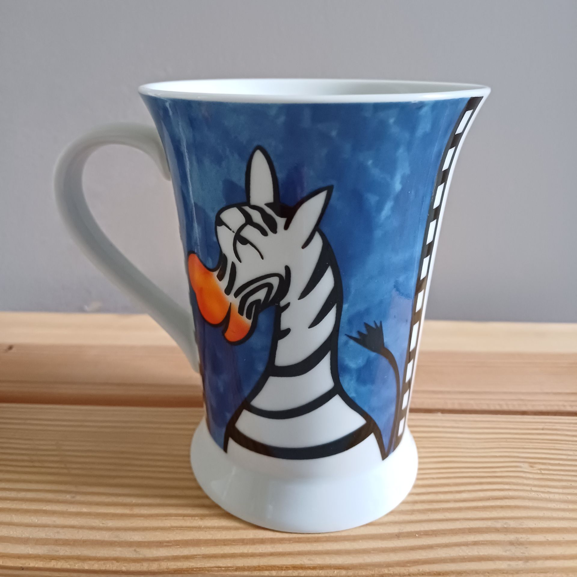 Mok met een cartoonzebra op een blauwe achtergrond, met een oranje snavel.