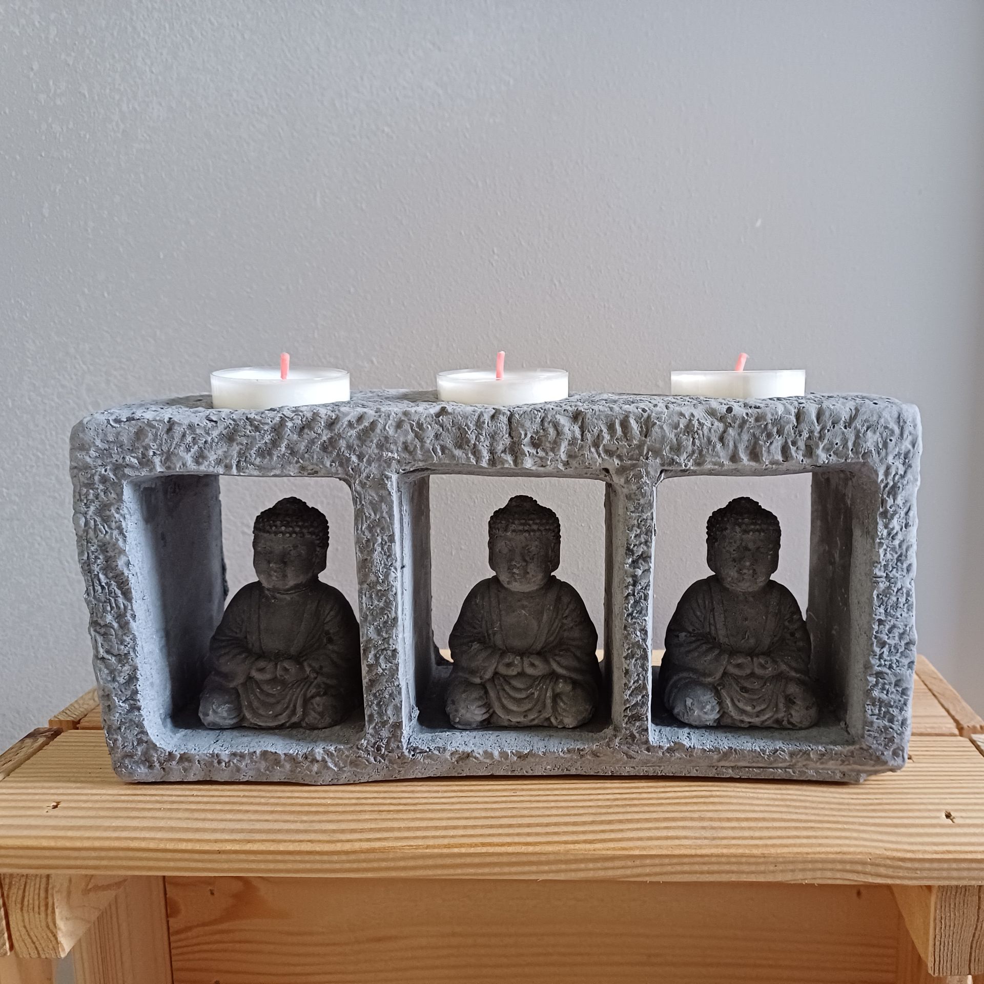 Boeddhabeeldje als kaarsenhouder: drie stenen Boeddha's in een grijs blok met kaarsen erop, op een houten plank.