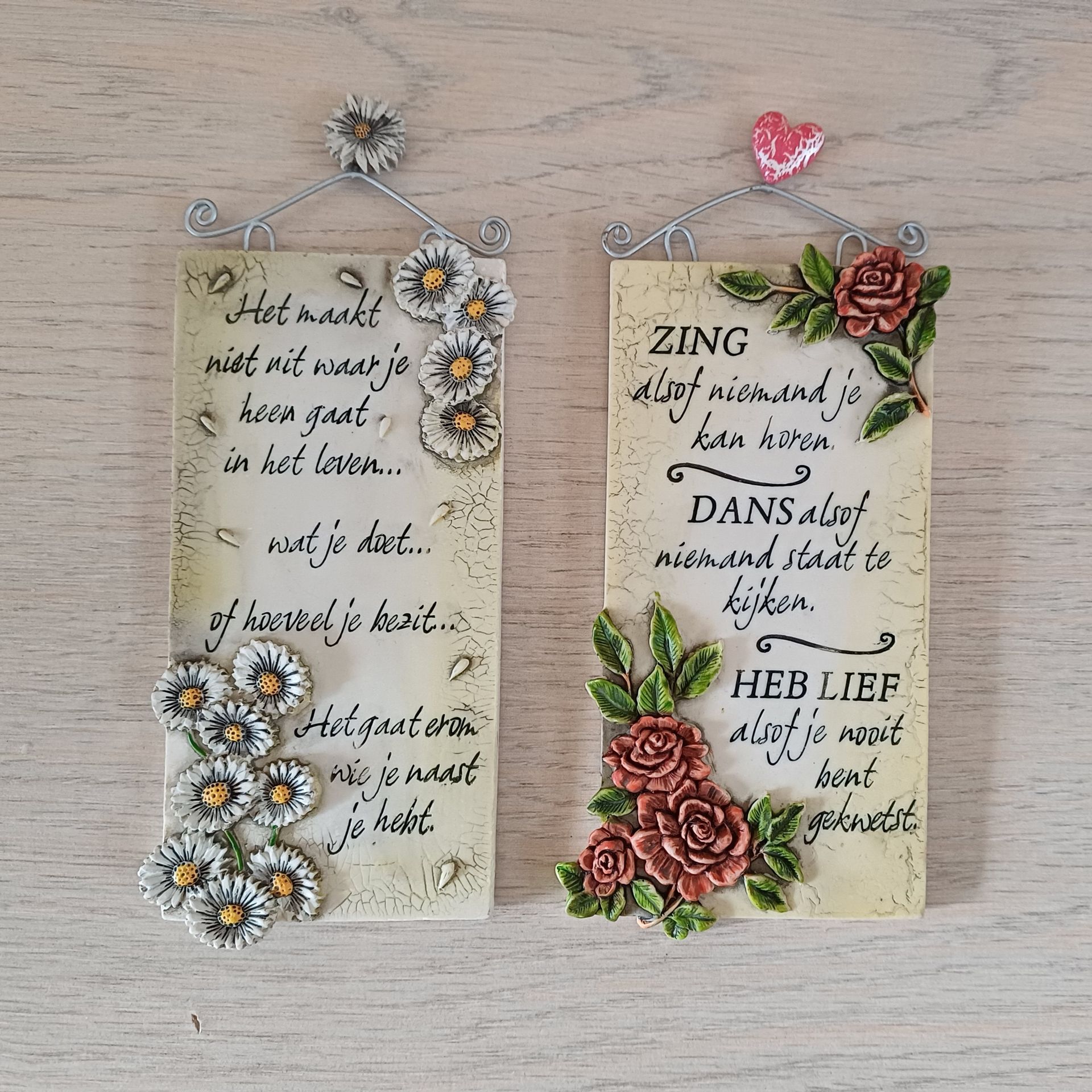 Twee decoratieve plaquettes met tekst en bloemversieringen.