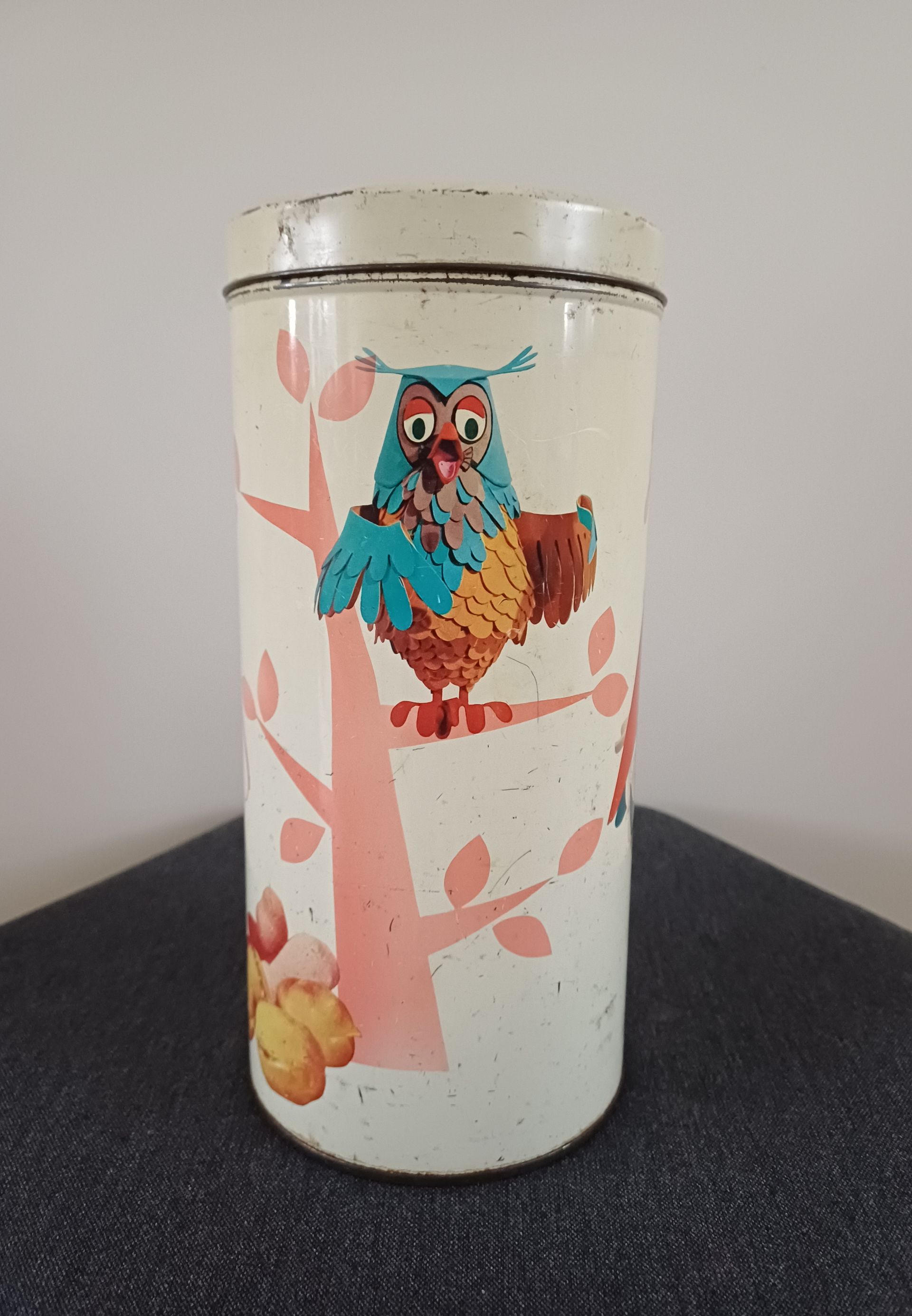 Blikje met een afbeelding van een uil die op een boomtak zit, wit, met een ronde bovenkant en een rode ruit erop.