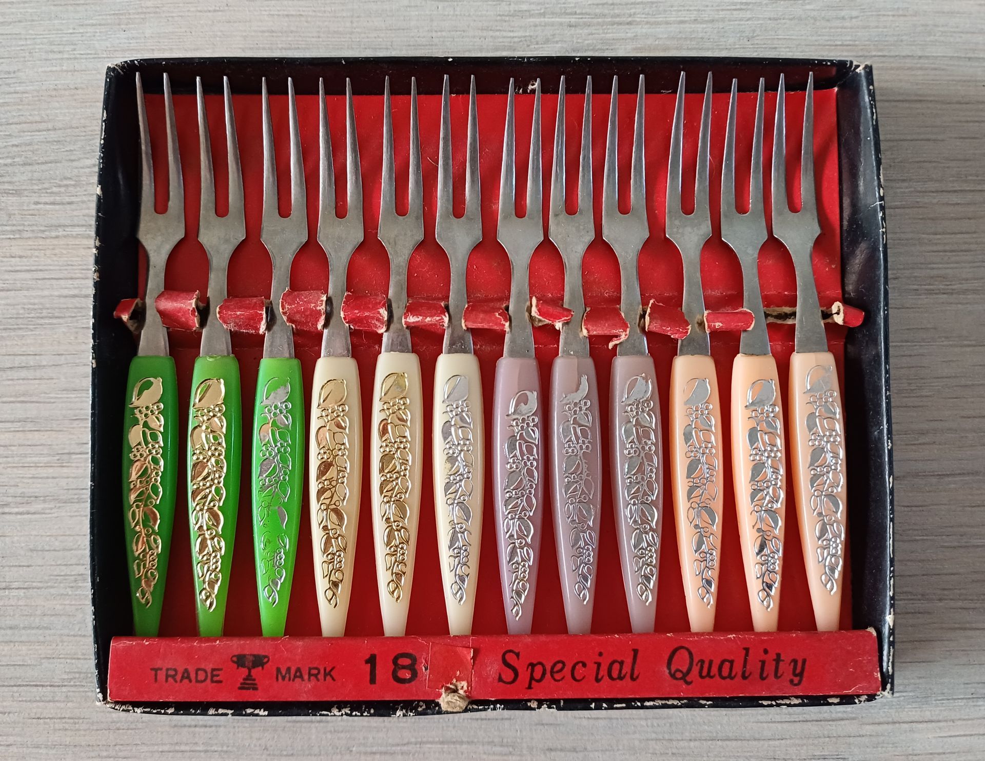Een doos met twaalf vintage cocktailvorkjes met kleurrijke handvatten; zwarte doos met rode binnenkant.