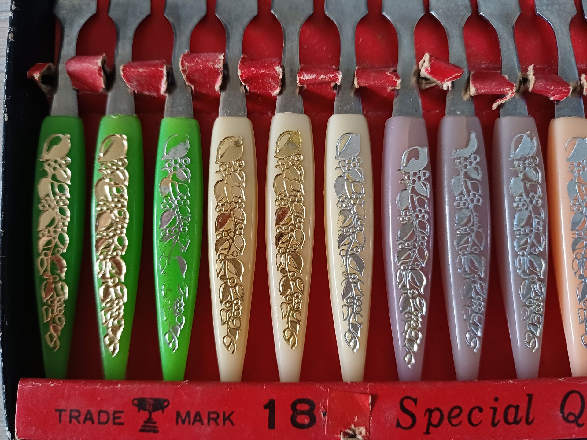 Een doos met twaalf vintage cocktailvorkjes met kleurrijke handvatten; zwarte doos met rode binnenkant.