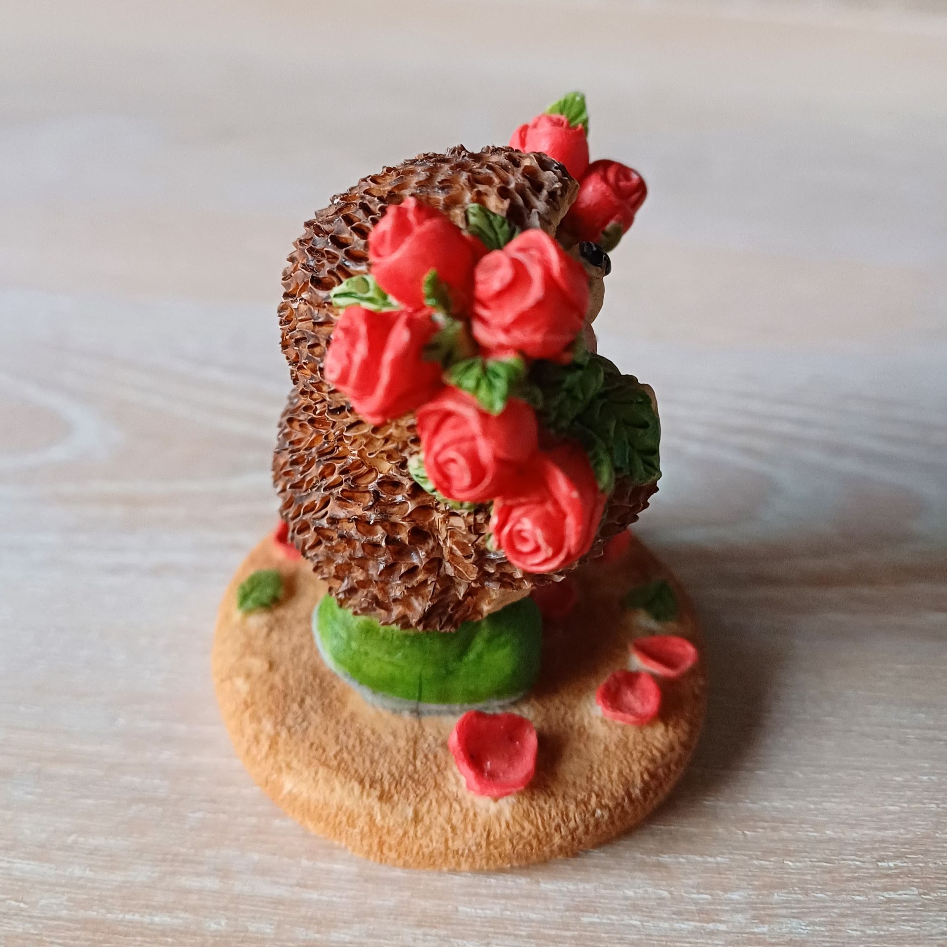 Egelfiguurtje met rode rozen op een bruine voet met groene laarsjes en rozenblaadjes.