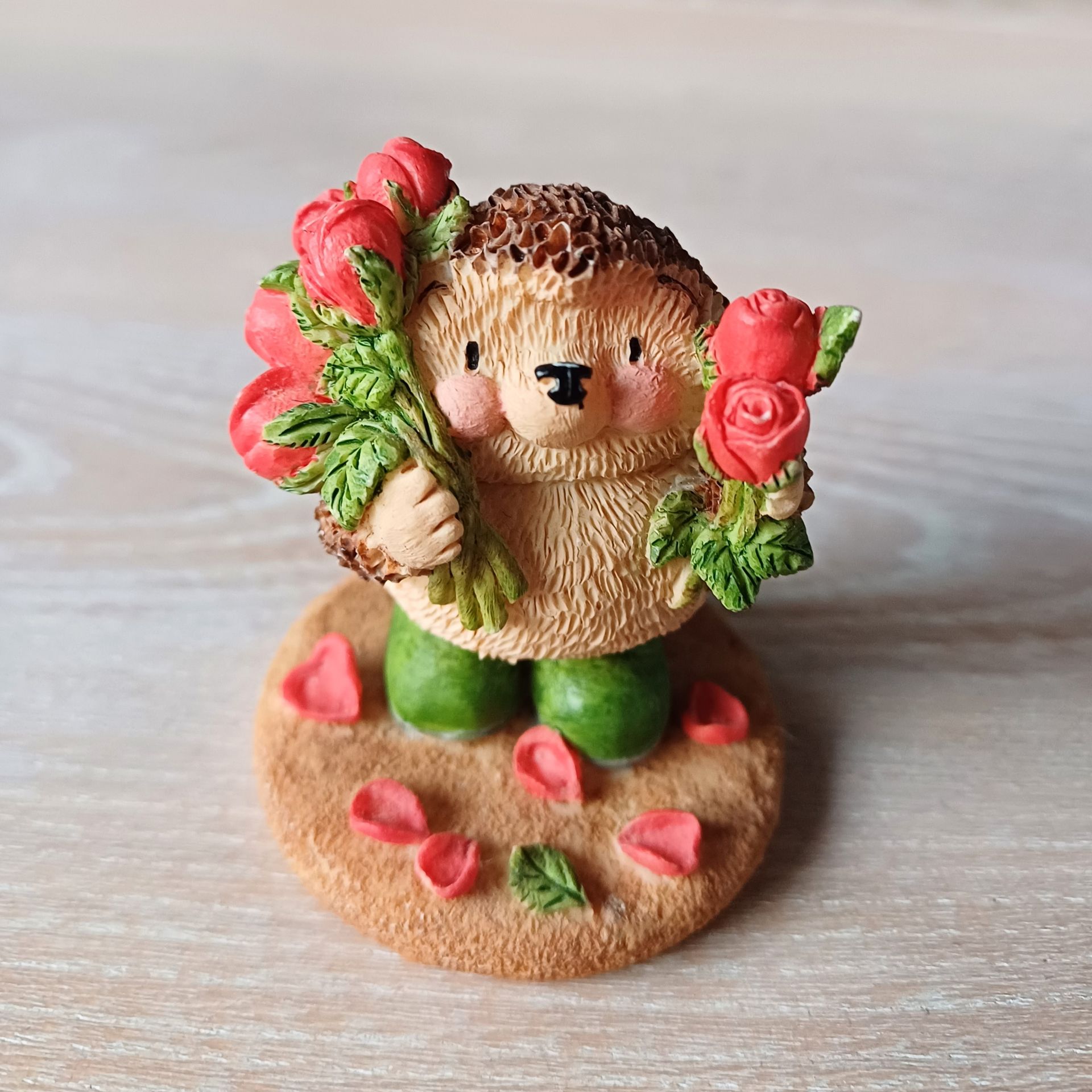 Egelfiguurtje met rode rozen op een bruine voet met groene laarsjes en rozenblaadjes.