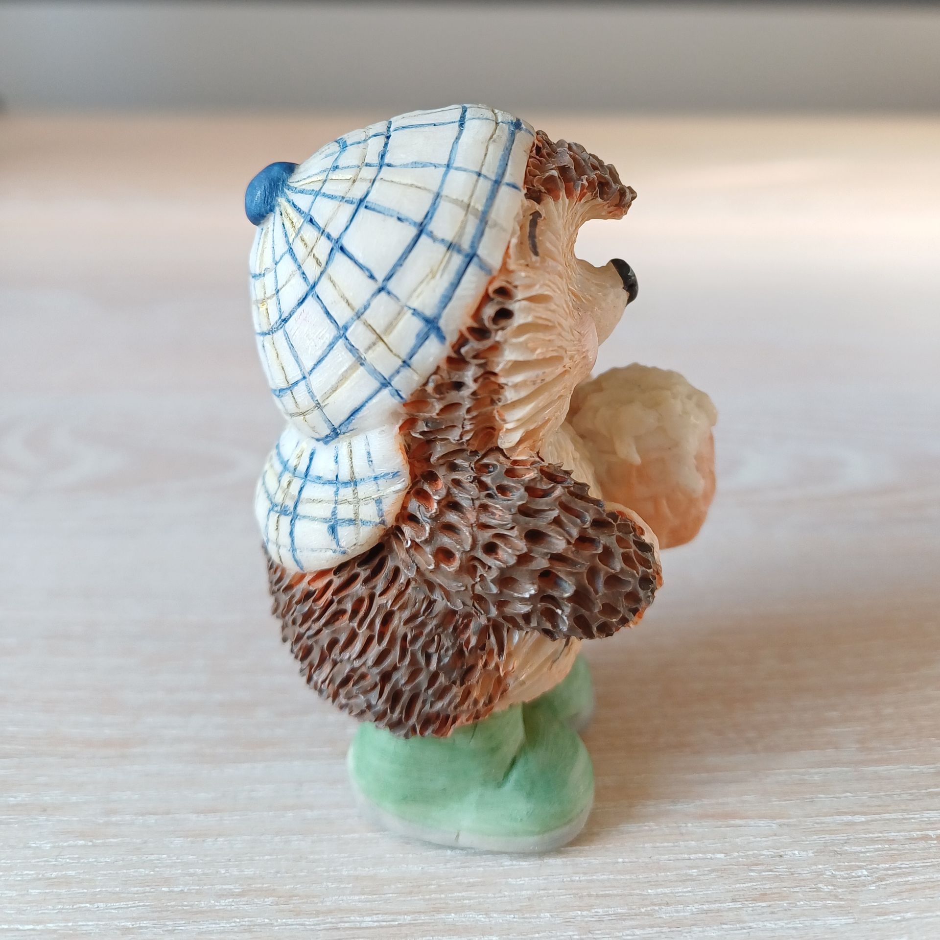 Beeldje van een egel die een honingraat vasthoudt, een hoed draagt ​​en groene laarzen aanheeft.
