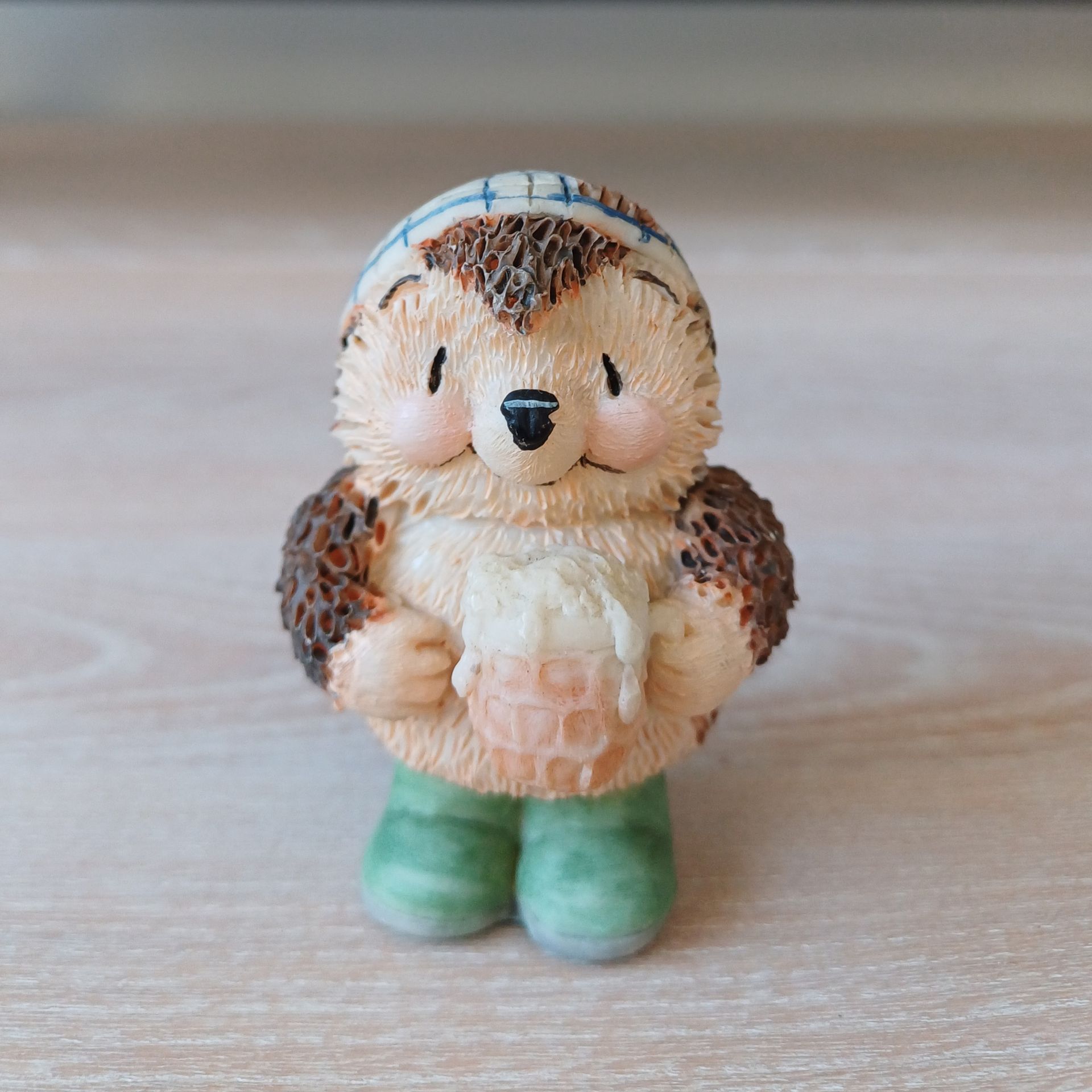 Beeldje van een egel die een honingraat vasthoudt, een hoed draagt ​​en groene laarzen aanheeft.