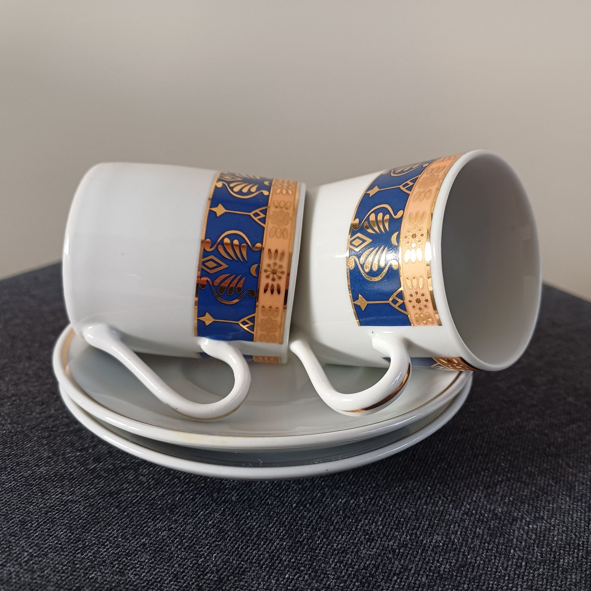 Koffiekopje en schoteltje van wit porselein met een decoratieve rand in goud en blauw.