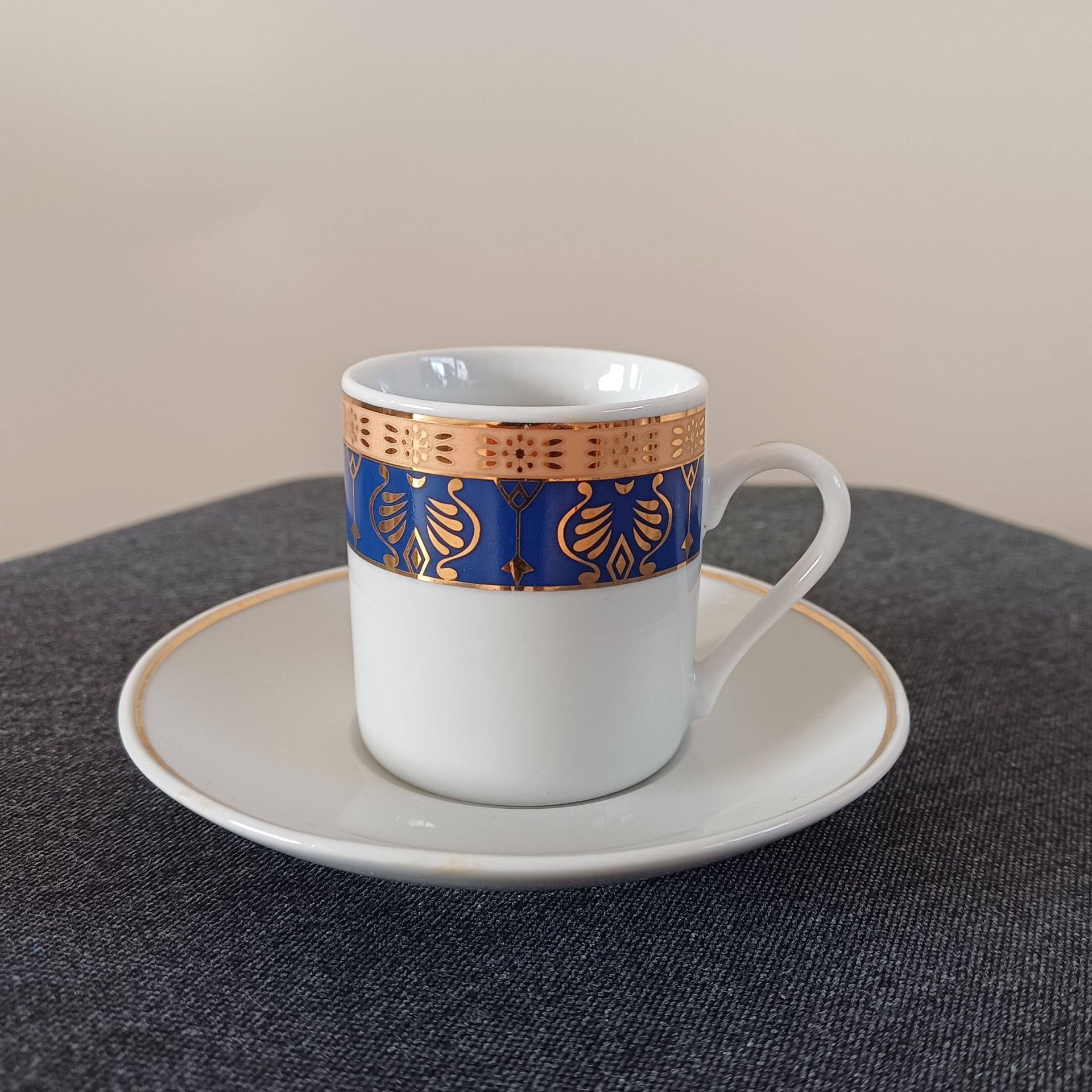 Koffiekopje en schoteltje van wit porselein met een decoratieve rand in goud en blauw.