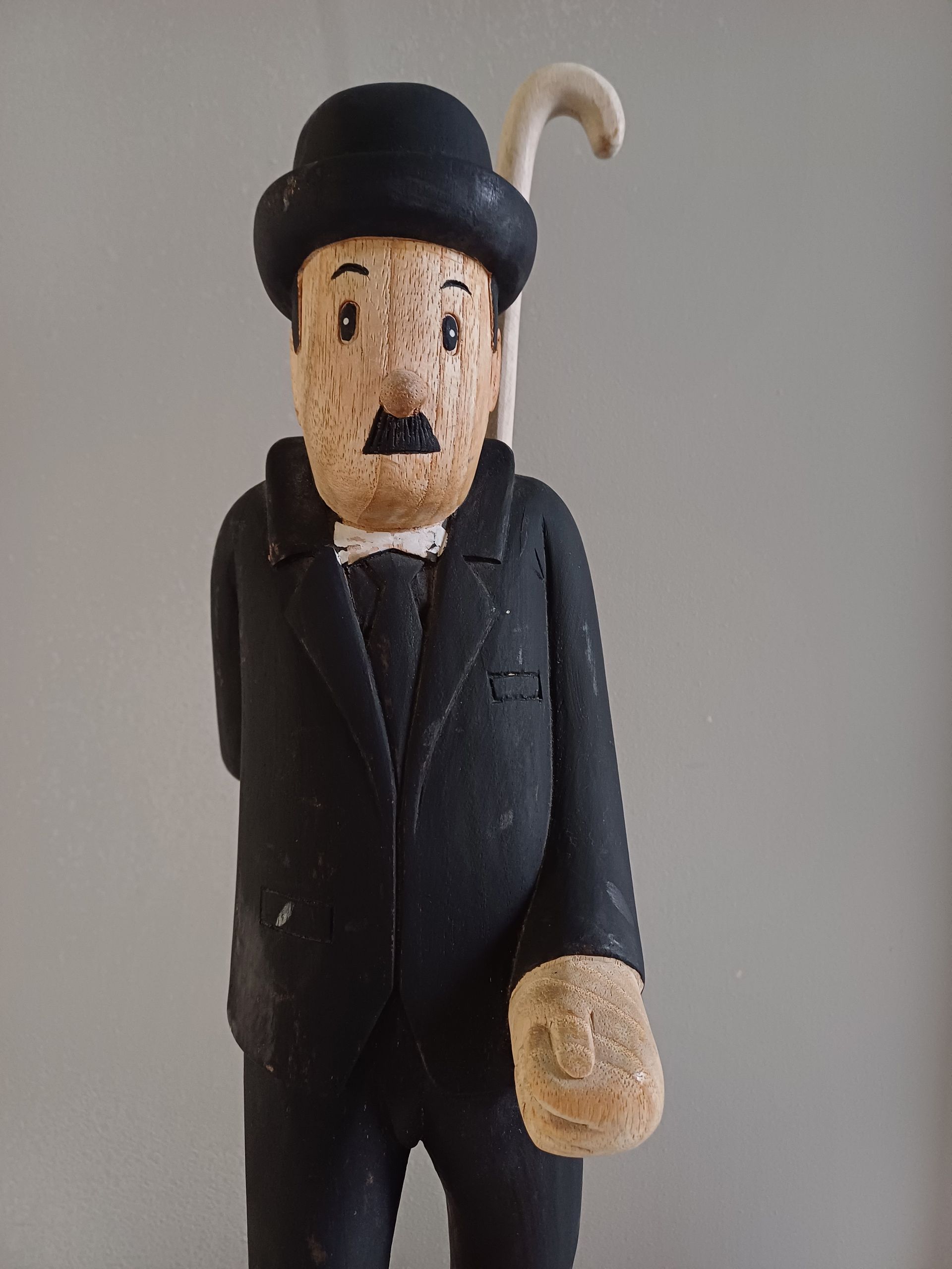 Houten beeld van Charlie Chaplin in een zwart pak, bolhoed en wandelstok.