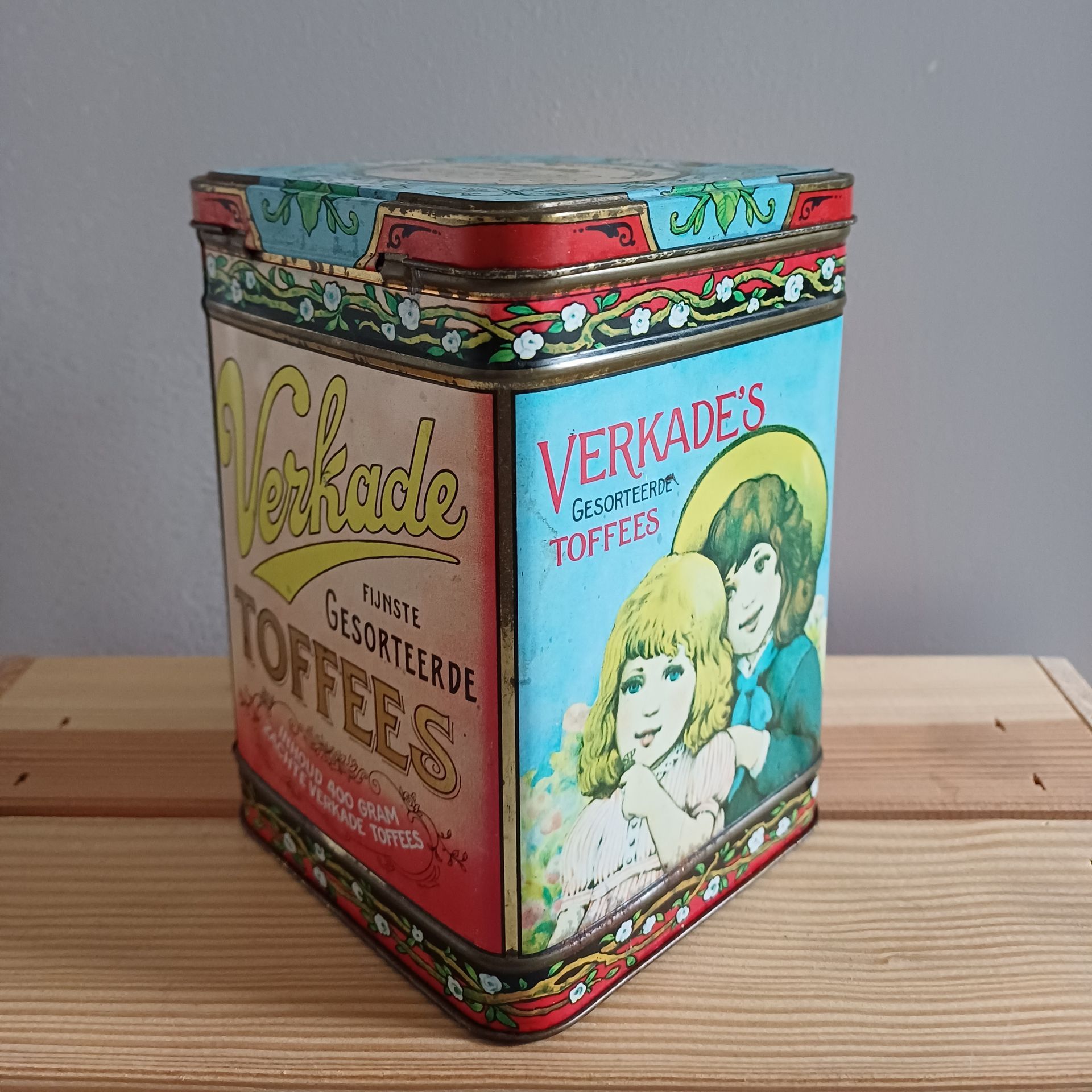Antieke Verkade toffeeblik met afbeelding van twee vrouwen. Rood, blauw en geel met bloemmotief.