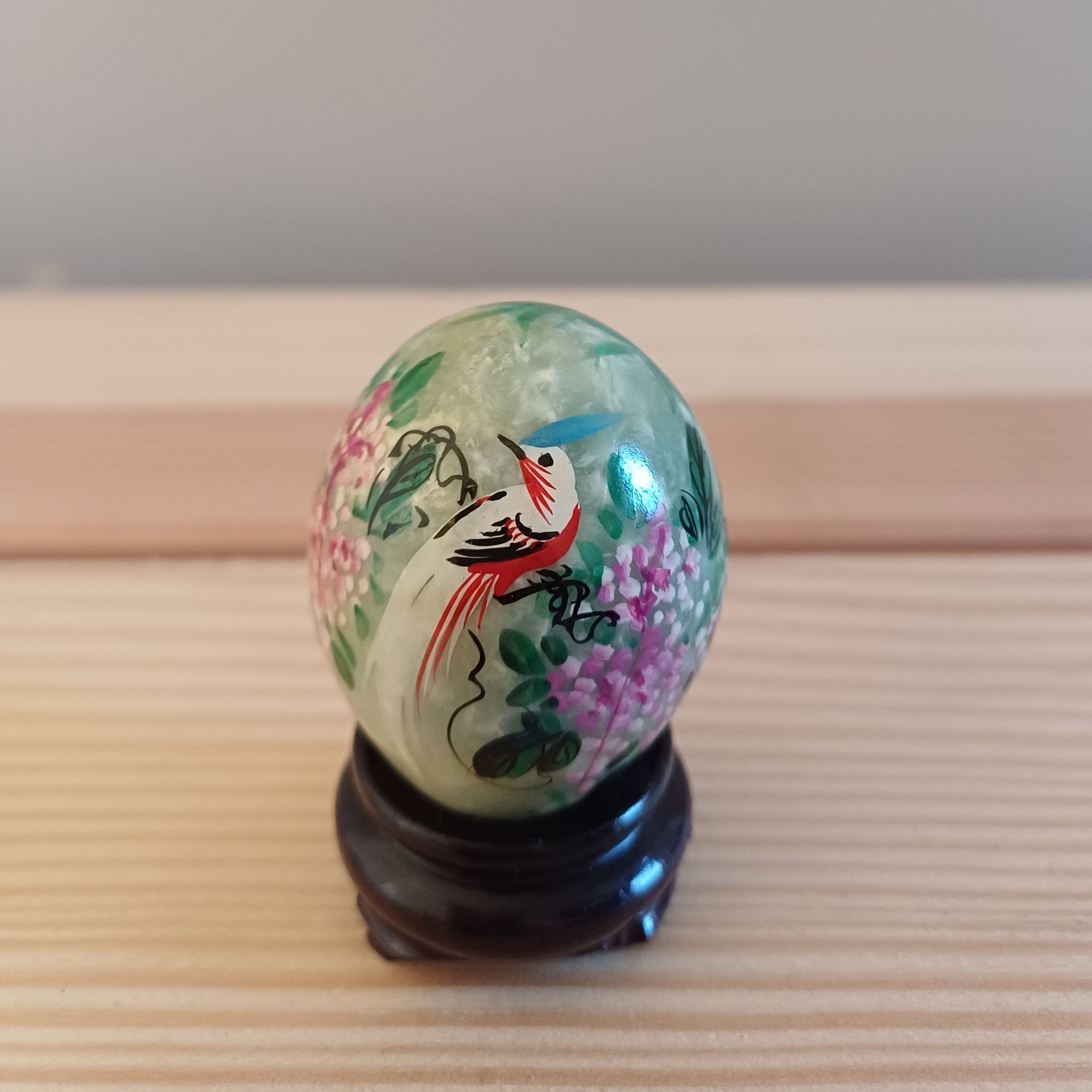 Jade-ei met beschilderde vogel en bloemen, op een zwarte standaard.