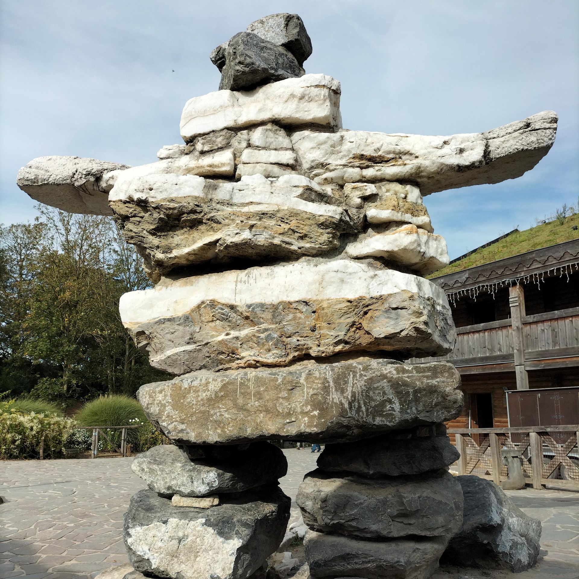 Inuksuk-sculptuur gemaakt van opgestapelde grijze en witte stenen, met uitgestrekte armen, in de buitenlucht.