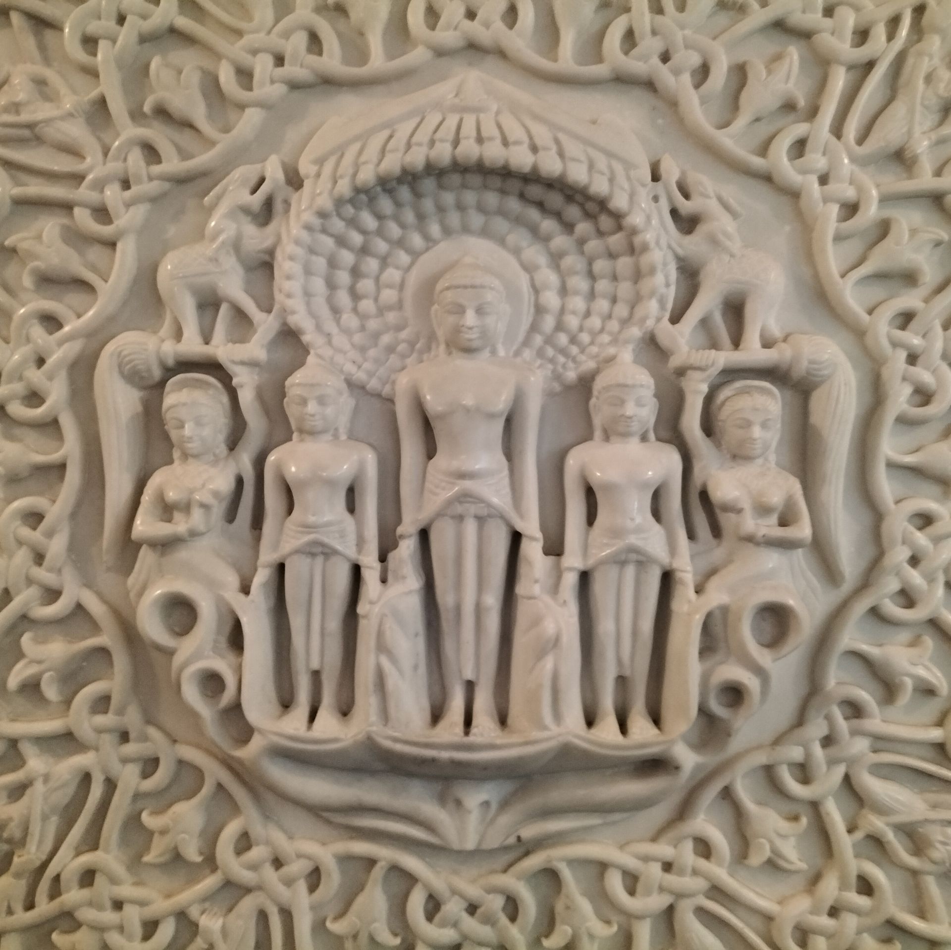 Reliëfsculptuur van wit marmer met afbeeldingen van Jain-figuren en een ingewikkelde bloemenrand.